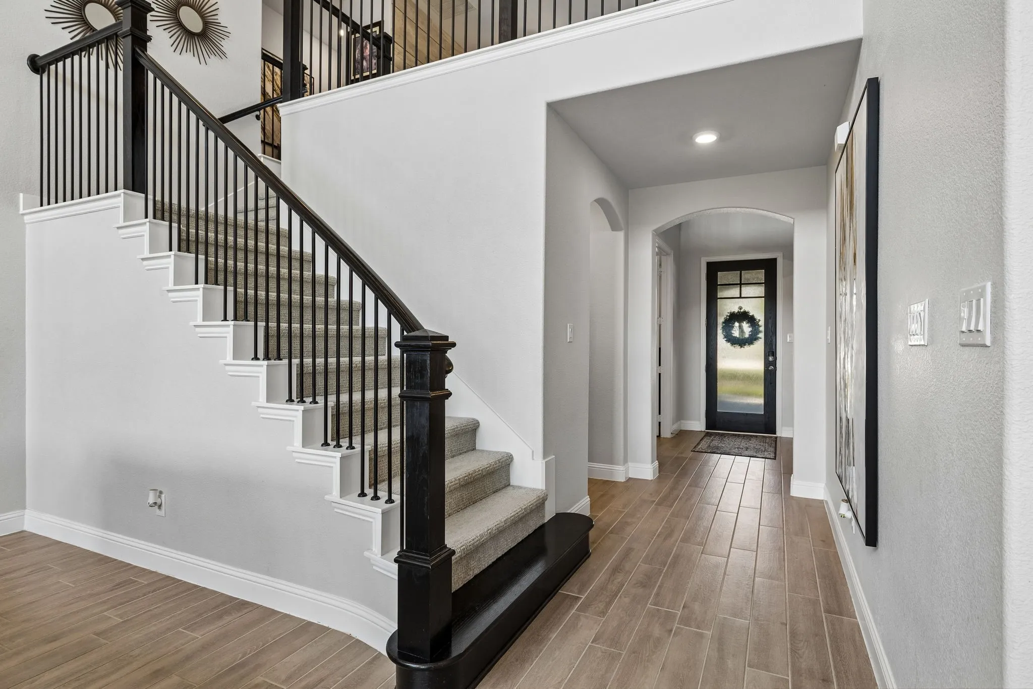 Dramatic entry welcomes guests with soaring ceilings, elegant arched passageways, wood-look tile flooring, and a striking staircase accented by black wrought-iron balustrades
