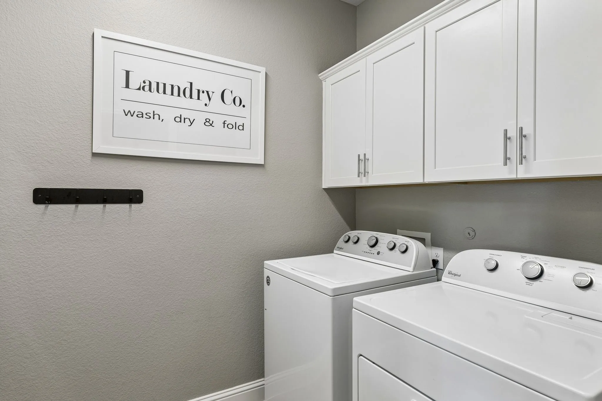Beautifully designed laundry room offers abundant custom cabinetry, generous storage, classic white finishes, and a practical layout surrounding the washer and dryer.