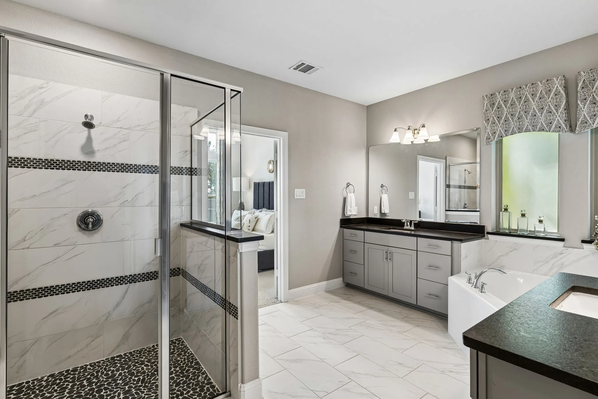 Beautifully appointed primary bath continues the home’s sophisticated aesthetic with marble-look surfaces, generous vanity storage, decorative window treatments, and abundant natural light.