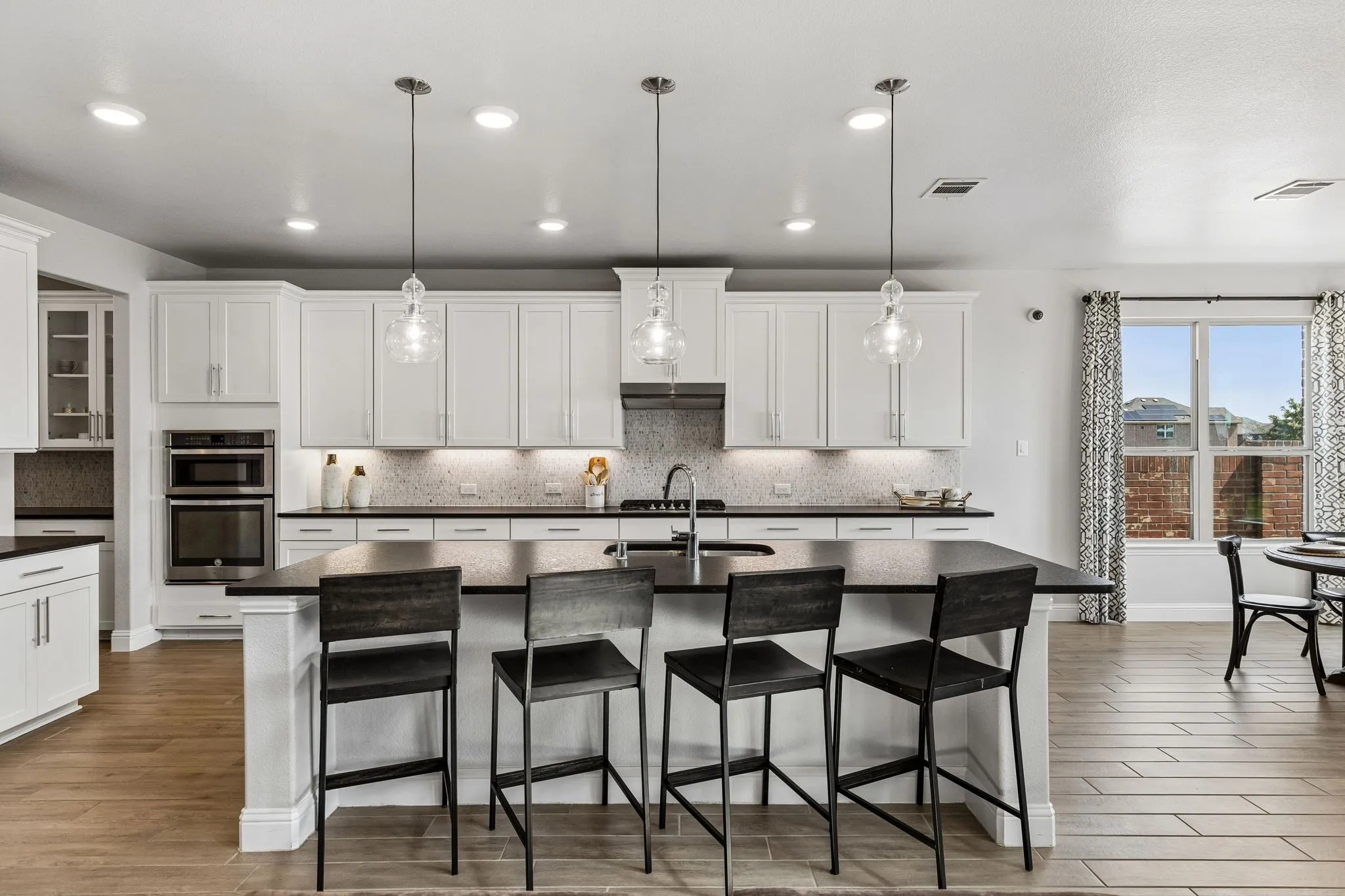 Gourmet-inspired kitchen features an abundance of crisp white cabinetry, generous dark countertops, subway-style mosaic backsplash, stainless appliances, oversized island, and ample workspace.