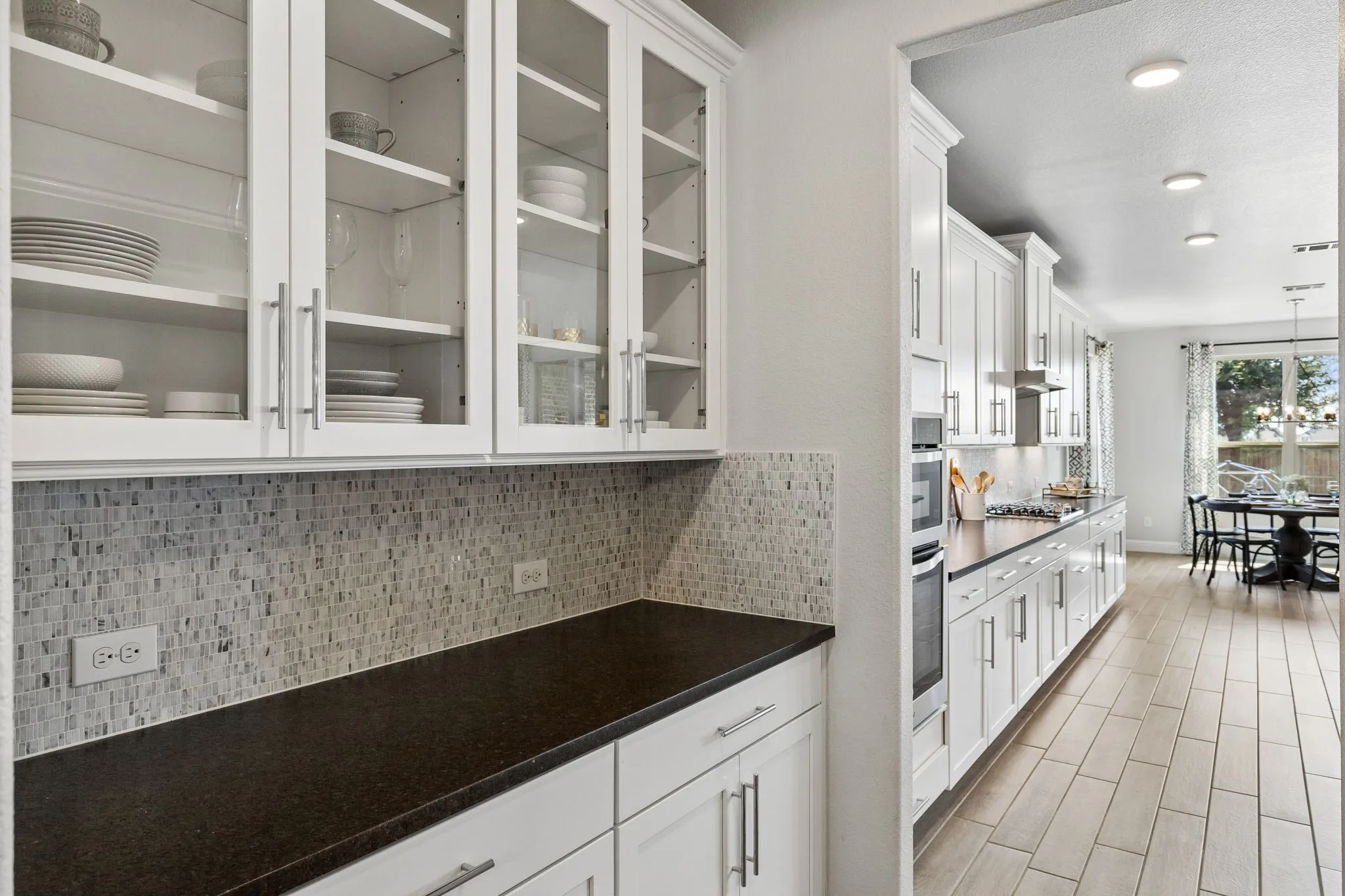 Thoughtfully designed butler's pantry that features glass-front cabinetry, extensive lower storage, elegant mosaic backsplash, and generous counter space for entertaining and everyday organization.