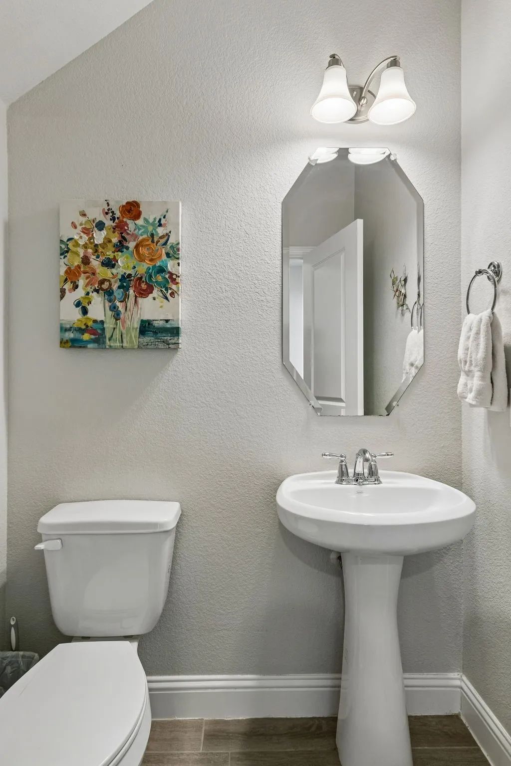 Charming powder bath is finished in a soft neutral palette with classic pedestal sink, decorative mirror, and crisp trim for an inviting touch.