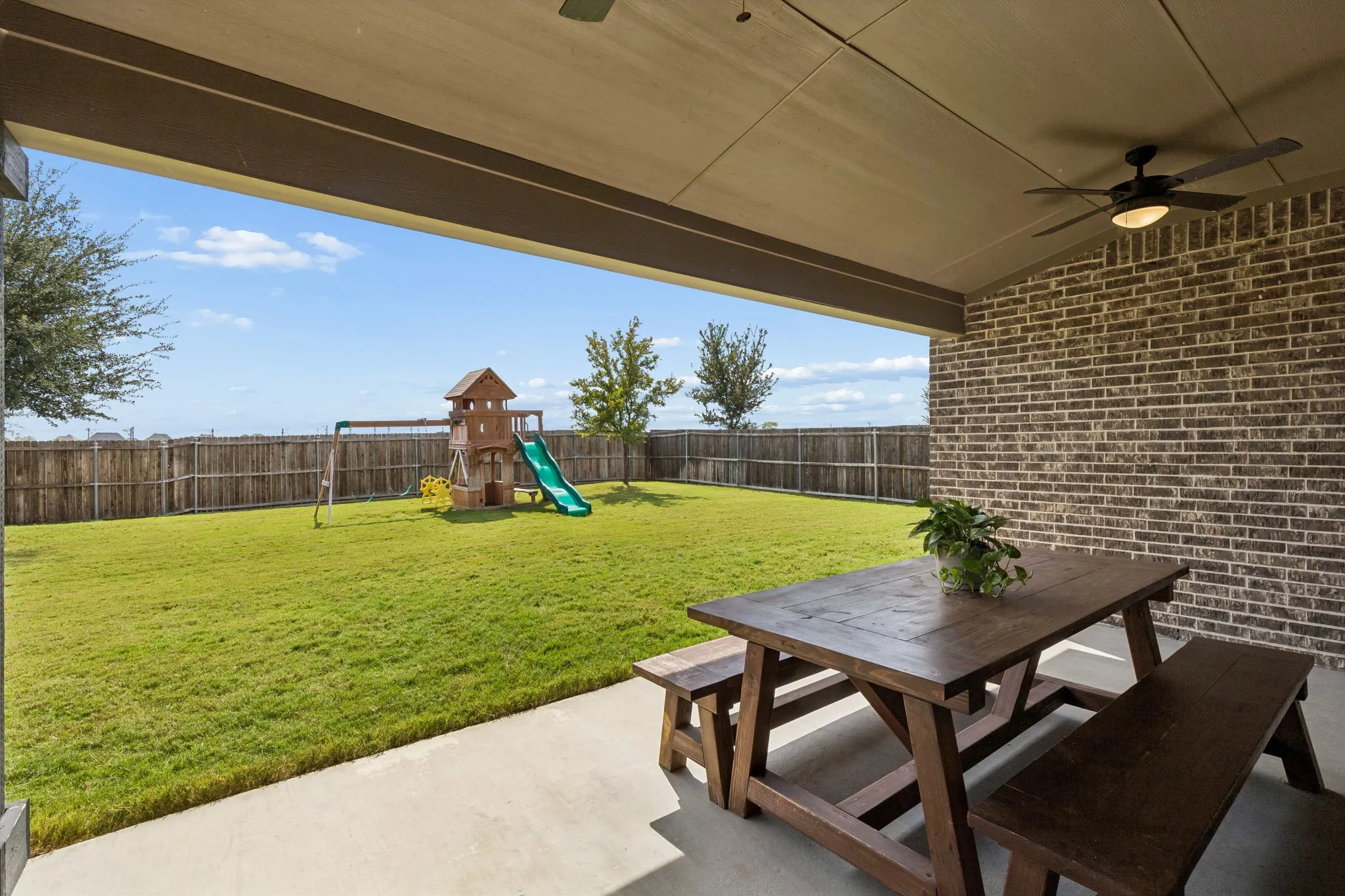 Expansive covered patio extends the home's living space outdoors, offering a generous area for dining, entertaining, and relaxing while overlooking the beautifully maintained backyard. A ceiling fan and substantial covered roofline provide added comfort for year-round outdoor enjoyment.