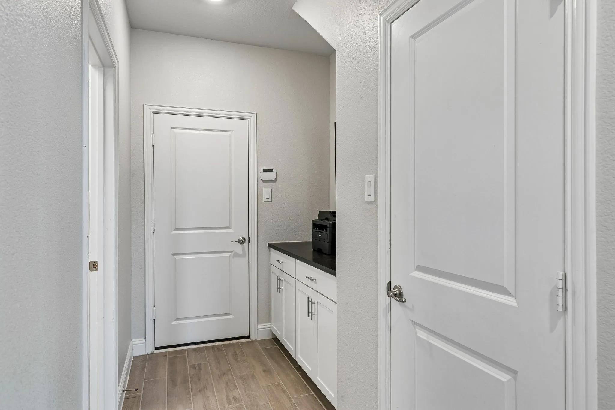 Mud Room showcases crisp white paneled doors, soft neutral walls, warm wood-look flooring, and beautifully appointed built-in cabinetry with a sleek dark countertop, creating a polished and highly functional transition into the home's utility spaces.