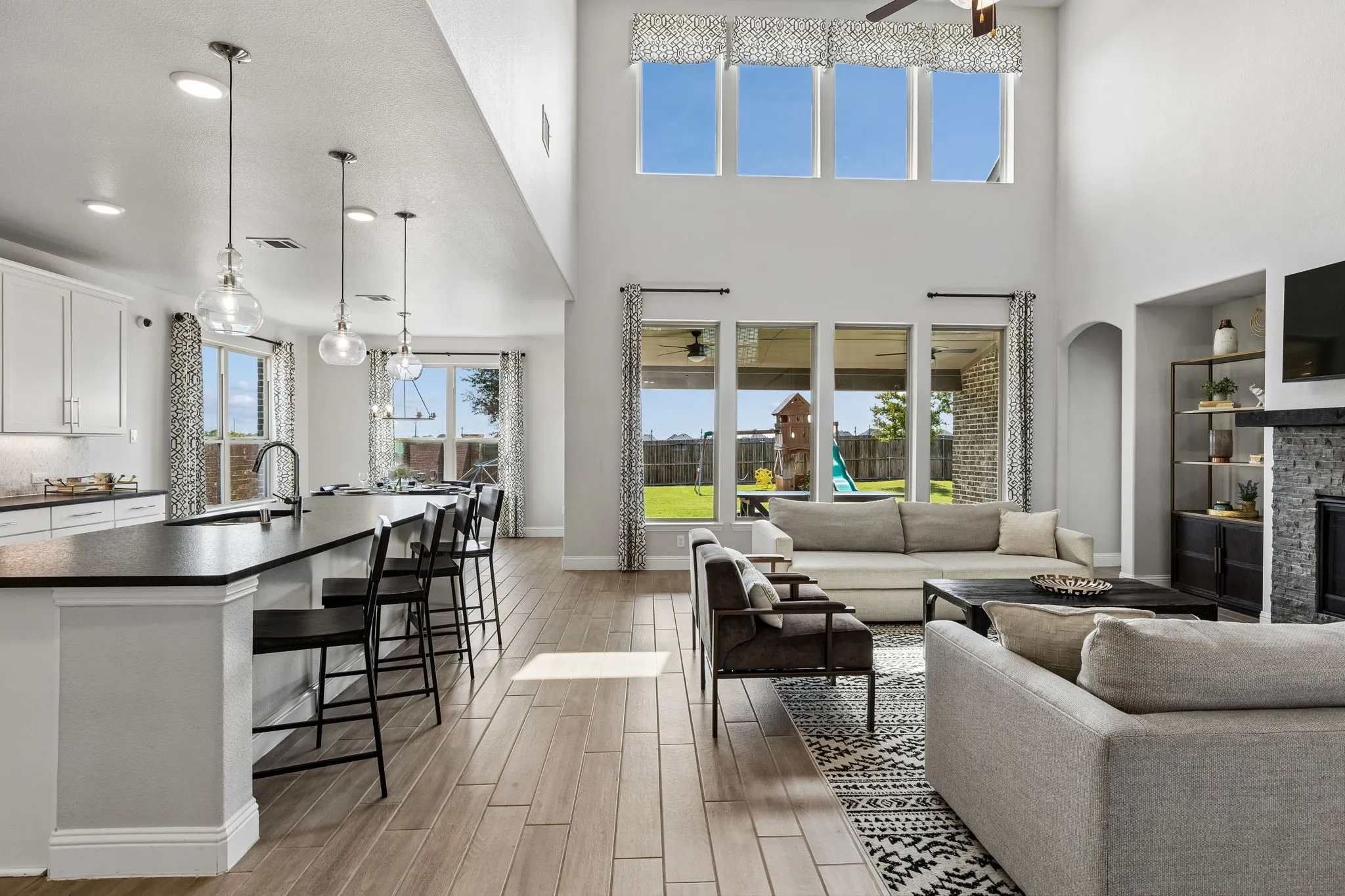 Impressive open-concept living space seamlessly connects the living room and kitchen, highlighted by soaring ceilings, expansive windows, abundant natural light, and effortless views toward the backyard.