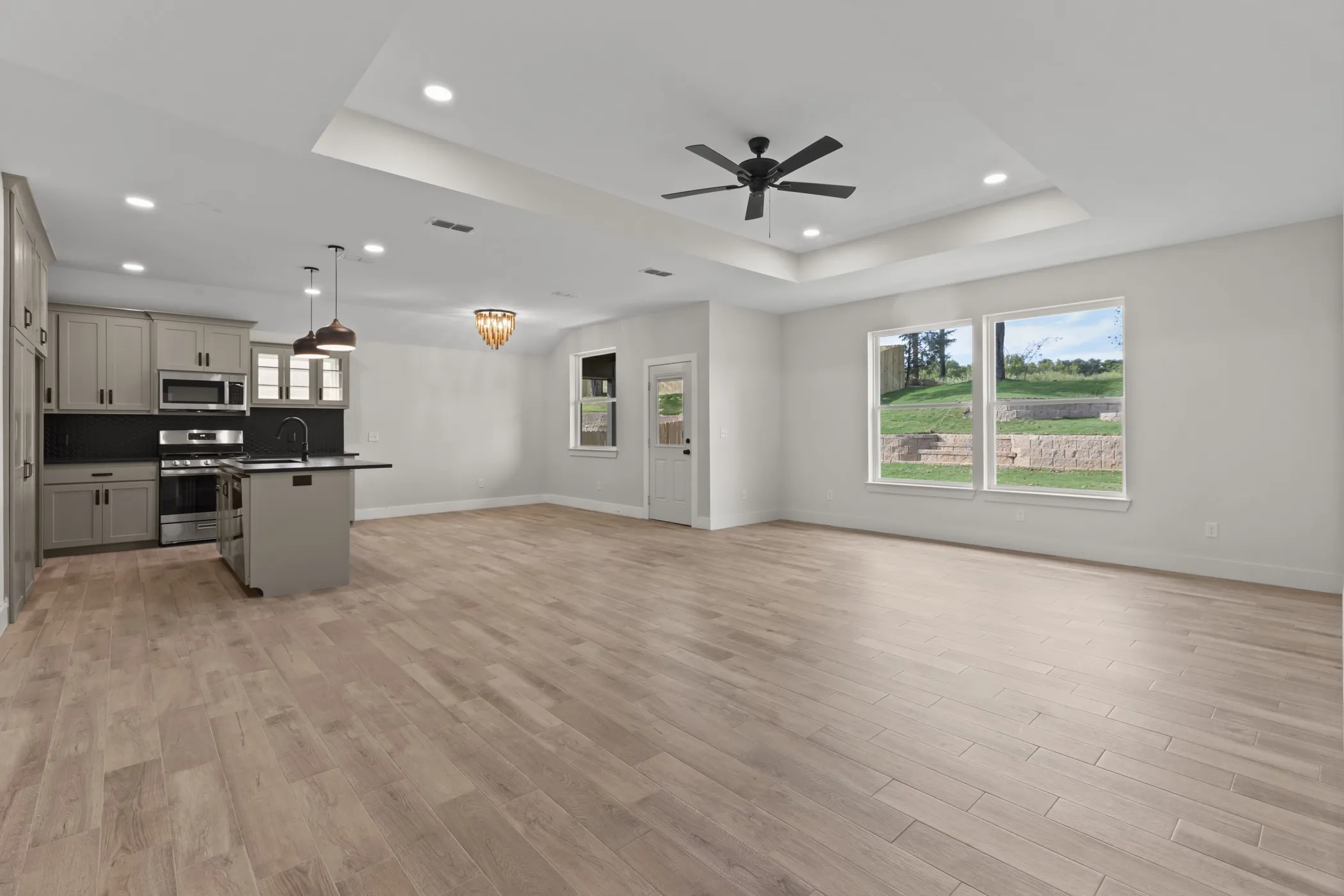 Open-concept living area with wood-finish flooring, a kitchen island, pendant lighting, and stainless steel appliances