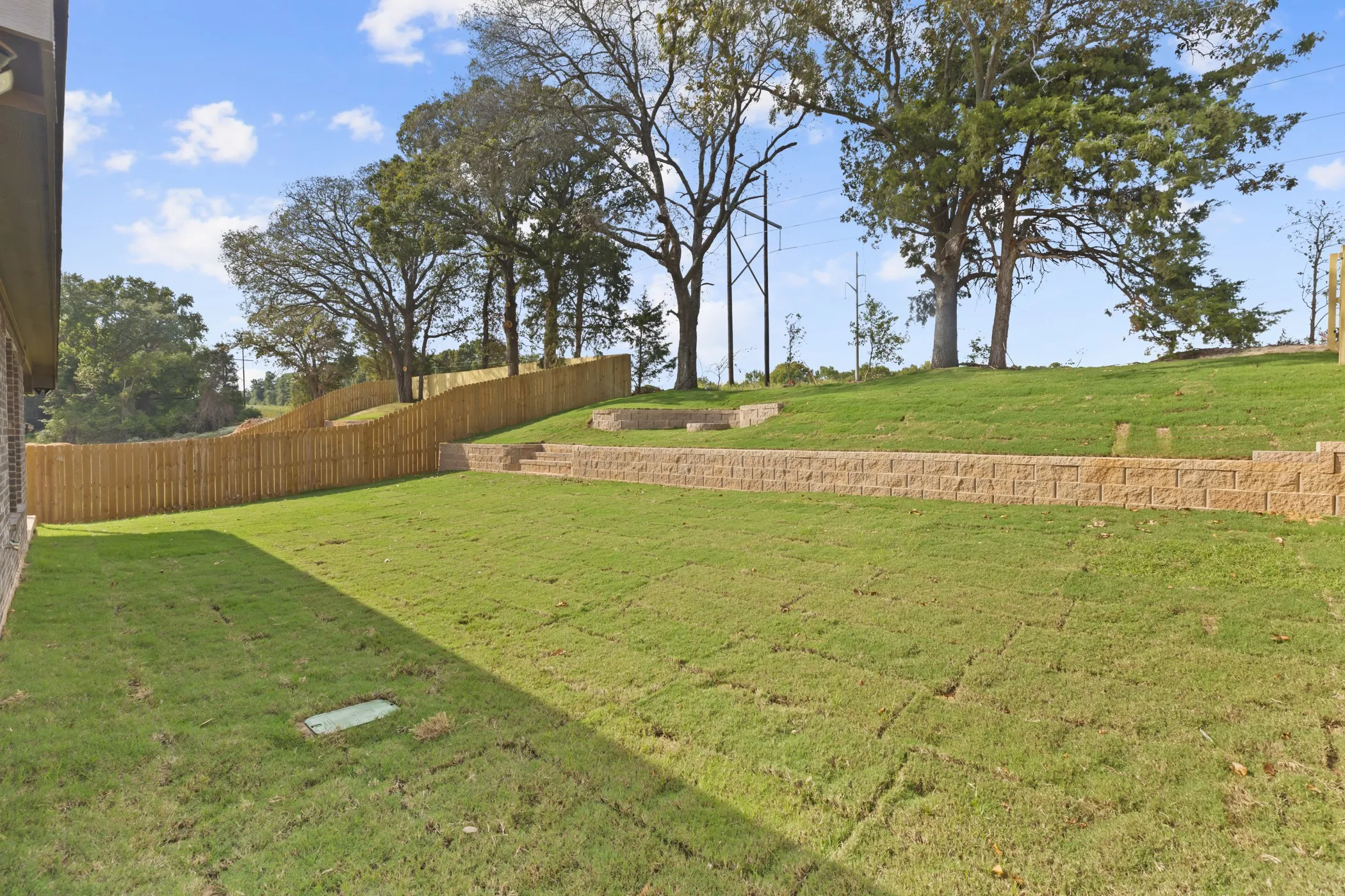 Expansive grassy yard featuring a new privacy fence and multiple retaining walls with integrated steps