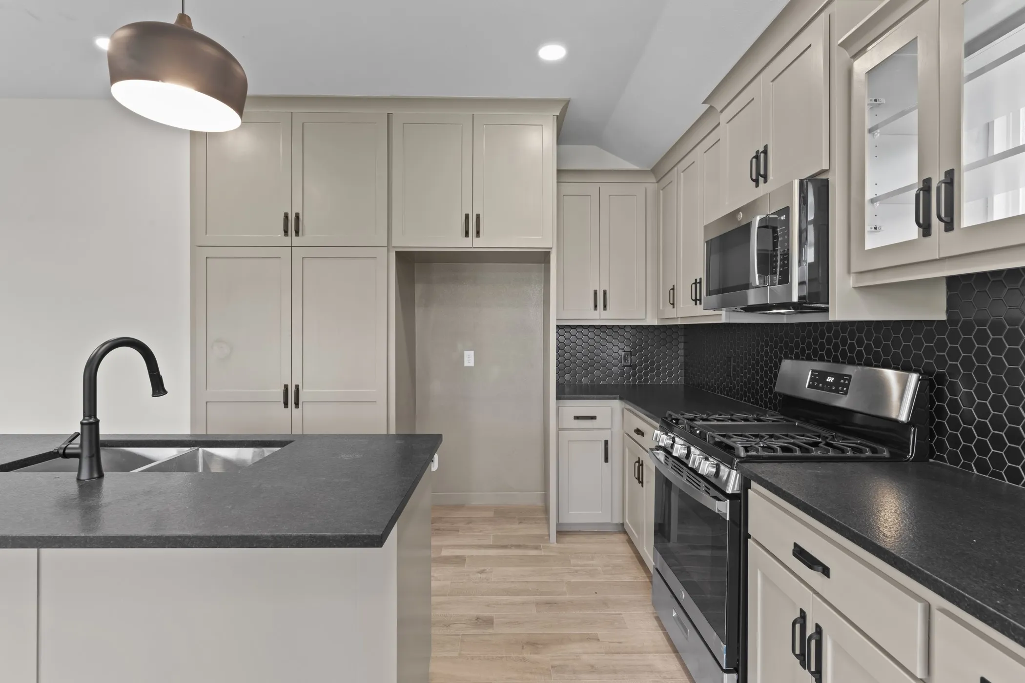 Contemporary kitchen featuring light-colored cabinetry, dark countertops, a black hexagonal tile backsplash, a stainless steel gas range, and a stainless steel built-in microwave