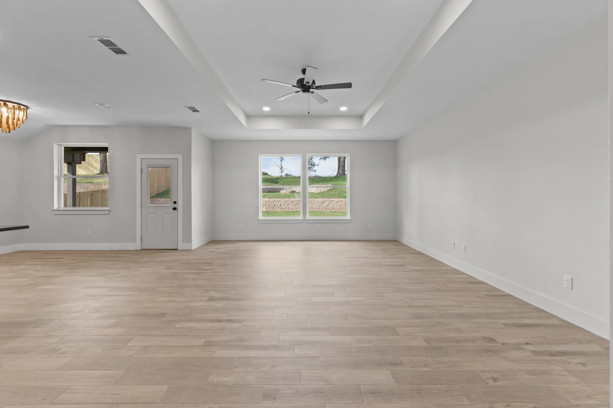 Spacious interior with wood-finish flooring, white walls, and a tray ceiling featuring a ceiling fan