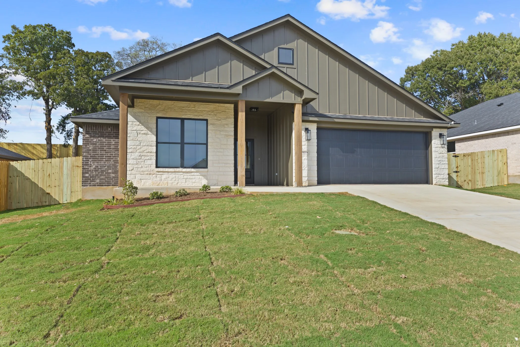 Stone and vertical siding exterior with wood-wrapped columns, a dark garage door, and a concrete driveway