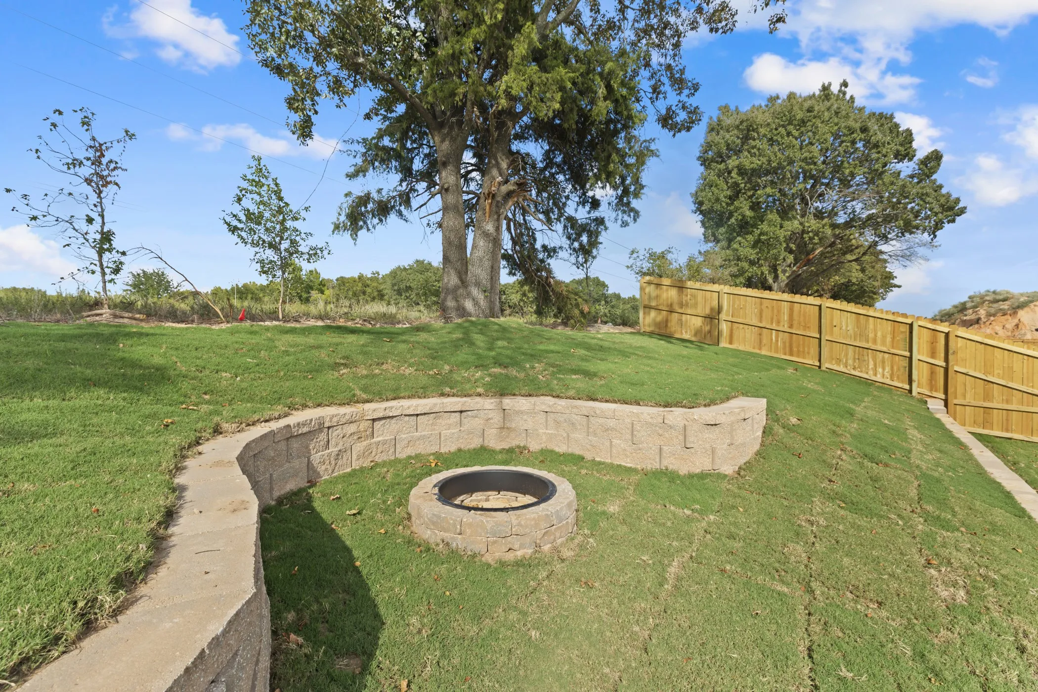 Expansive backyard featuring a manicured lawn, a stone retaining wall, and a built-in fire pit