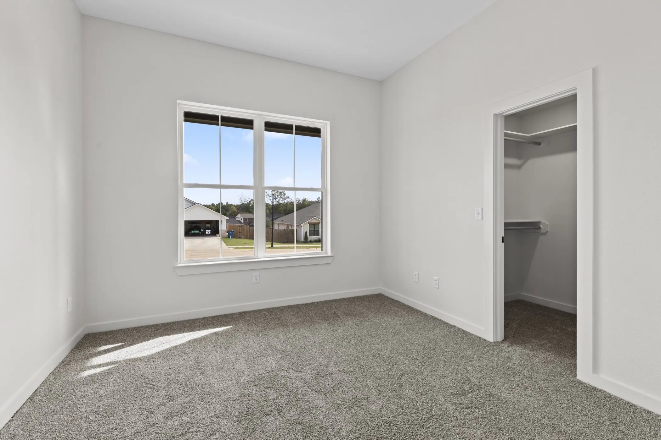 Carpeted room featuring a double window with exterior streetscape and a walk-in closet with built-in shelving