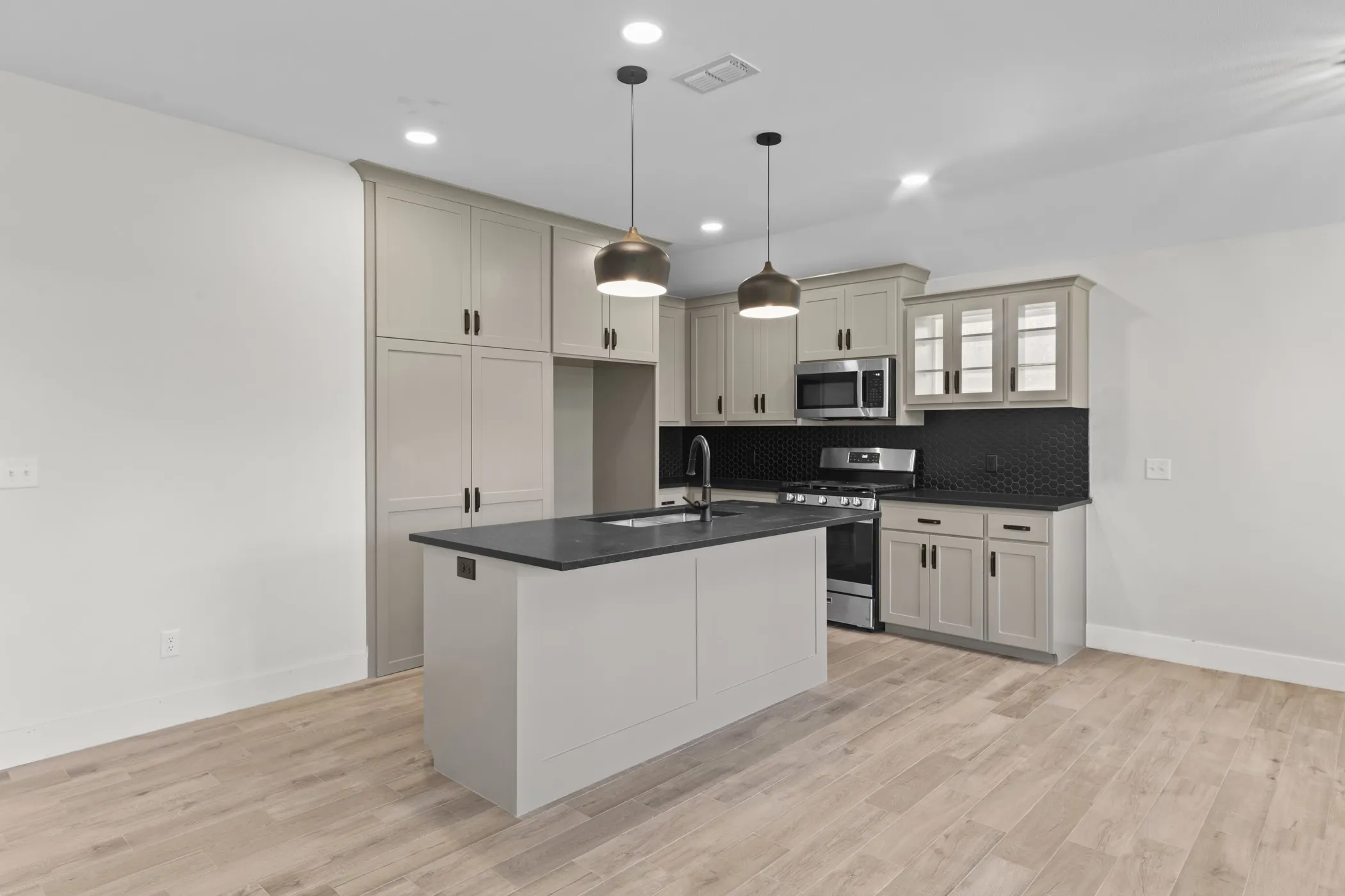 Kitchen featuring an island with a sink, recessed lighting, wood-finish flooring, full-height cabinetry, and stainless steel appliances