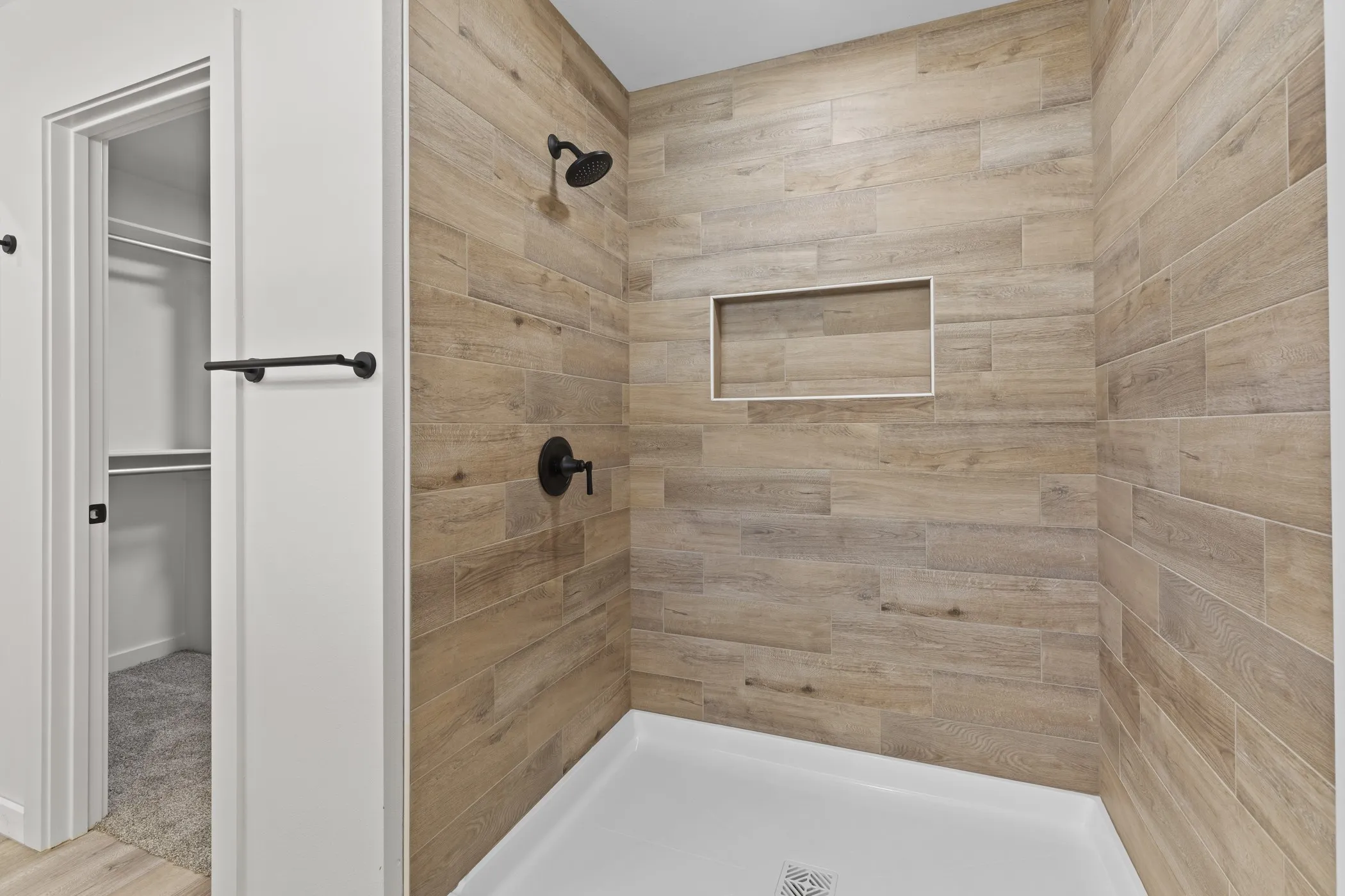 Shower featuring wood-finish tile walls, a built-in shower niche, and matte black fixtures