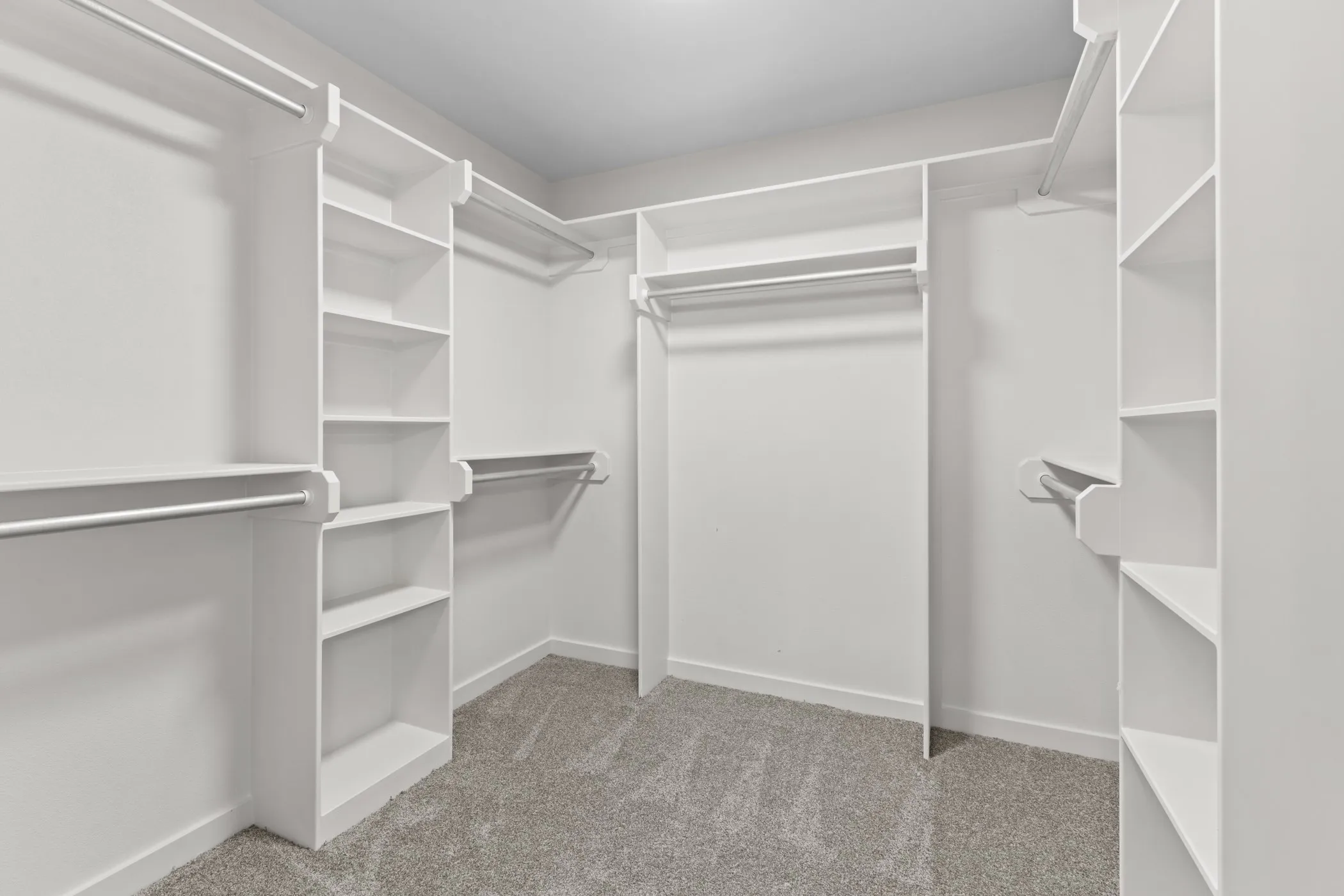 Built-in white shelving and hanging rods, recessed ceiling lighting, and gray carpet flooring