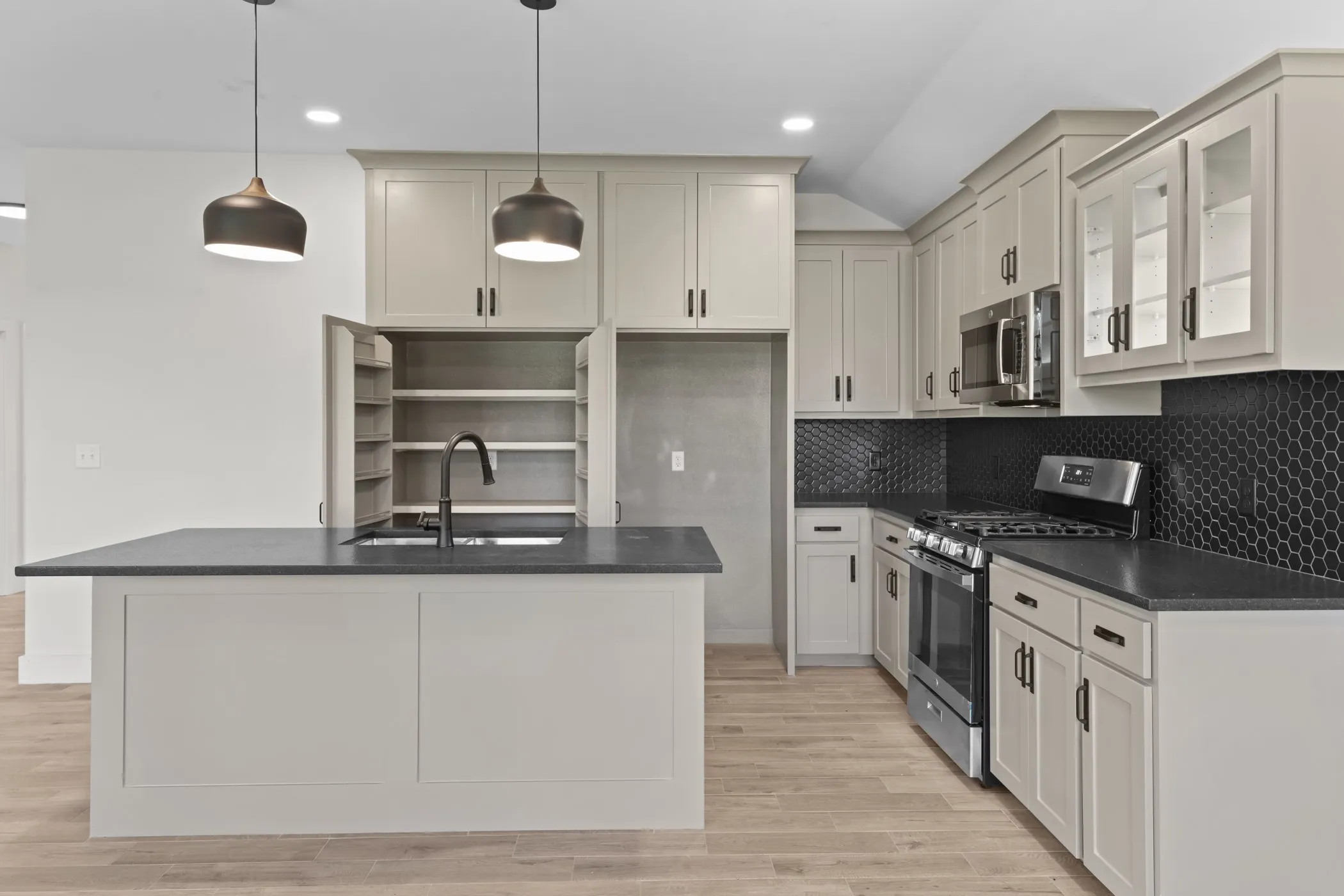 Kitchen featuring a central island with an undermount sink, pendant lighting, built-in pantry cabinetry, black hexagonal tile backsplash, and stainless steel appliances