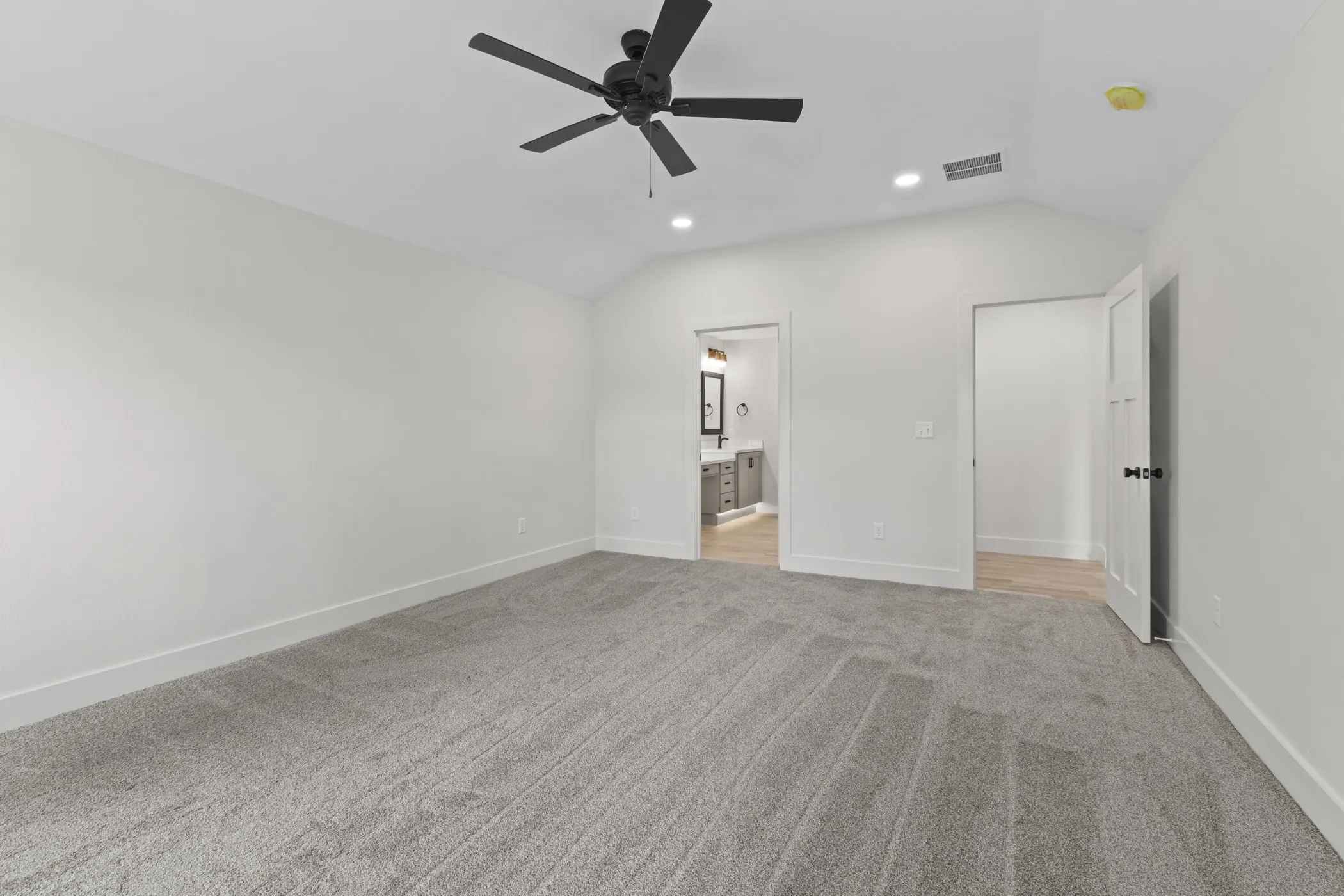 Vaulted ceiling with recessed lighting and a ceiling fan, carpeted flooring, and a door opening to a bathroom with a vanity and mirror