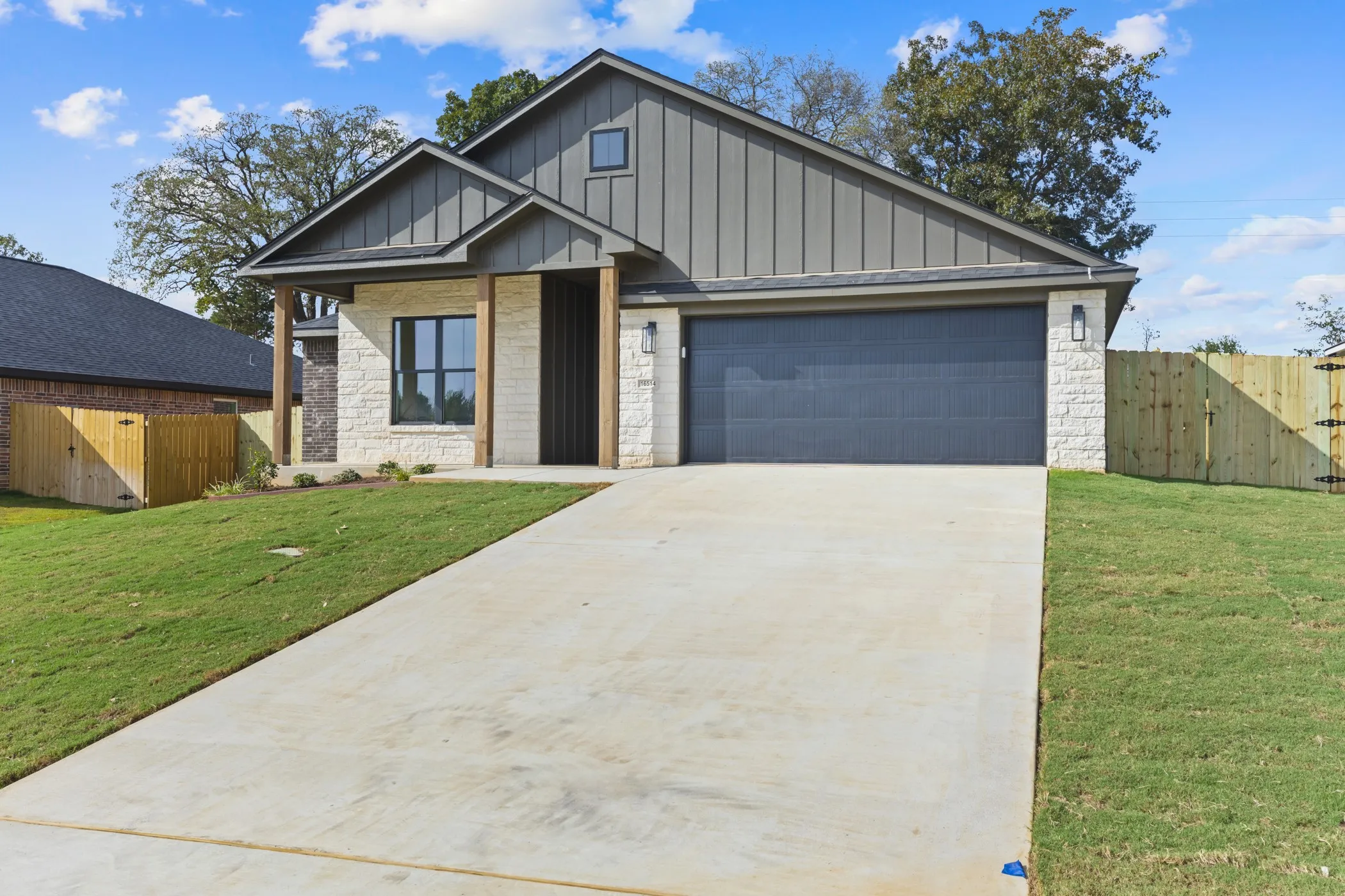 Contemporary exterior featuring vertical siding and stone accents, a deep gray garage door, a concrete driveway, wood support beams, and a wood privacy fence