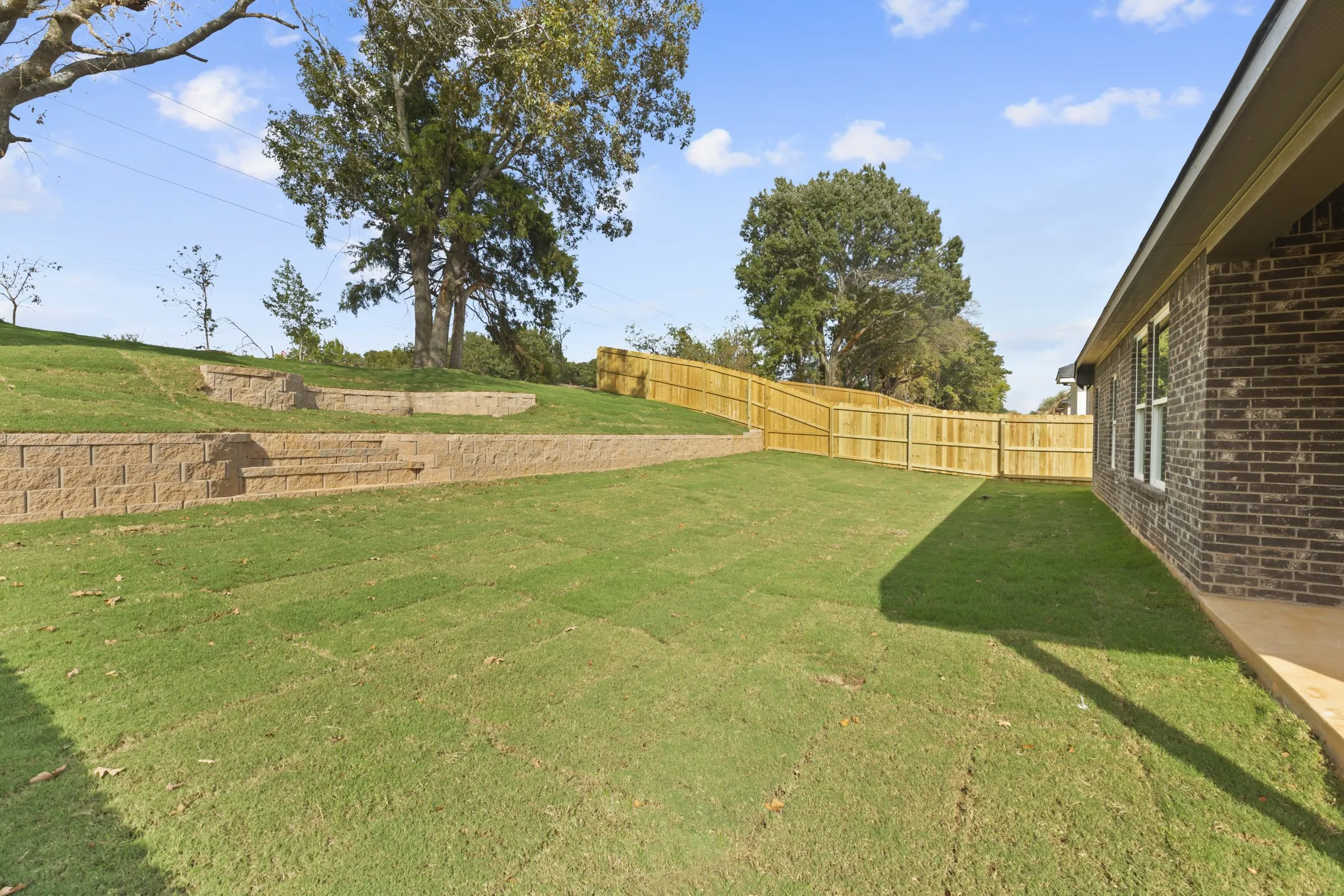 Expansive backyard with a level lawn, terraced retaining walls, and a wood privacy fence