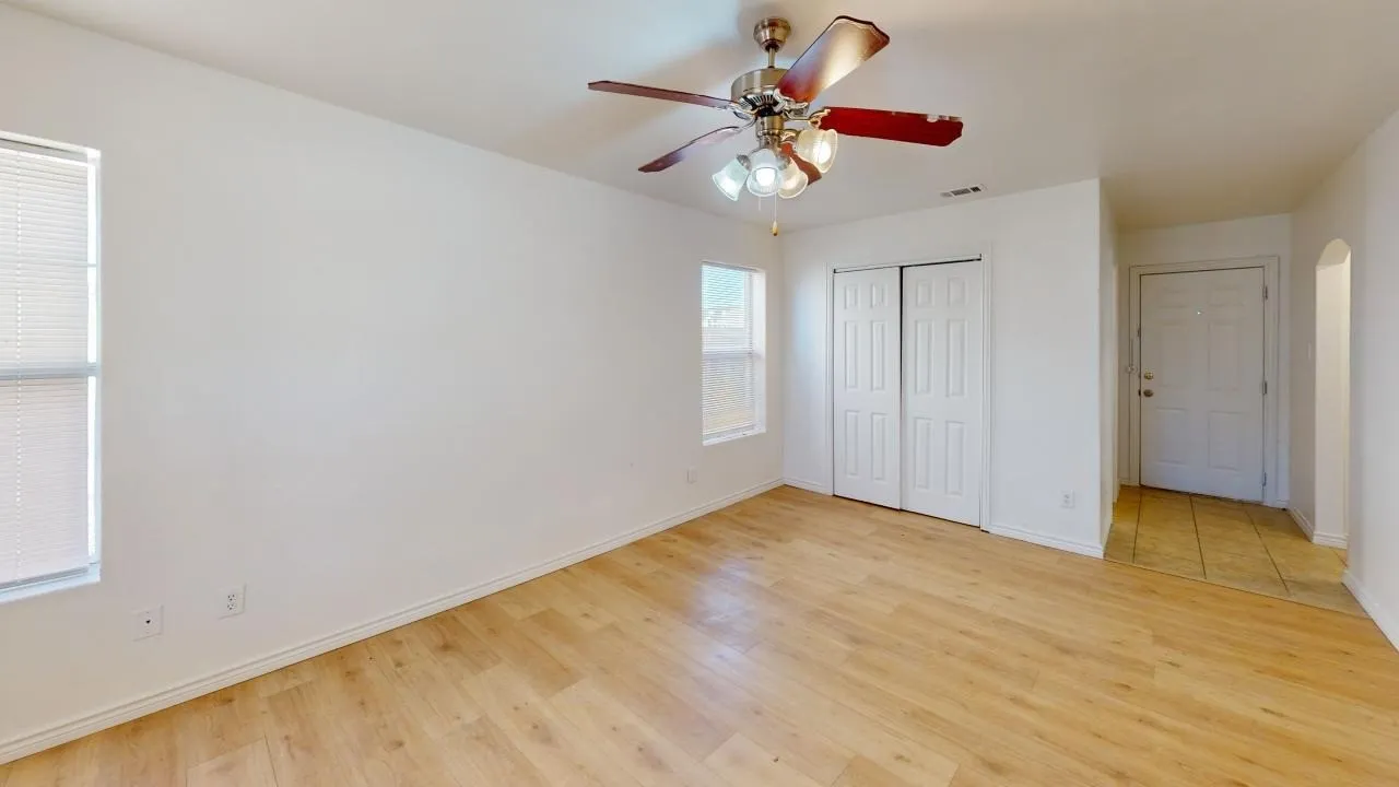 Wood-finish flooring, ceiling fan with integrated lighting, white bi-fold closet doors, white paneled entry door, and an arched doorway