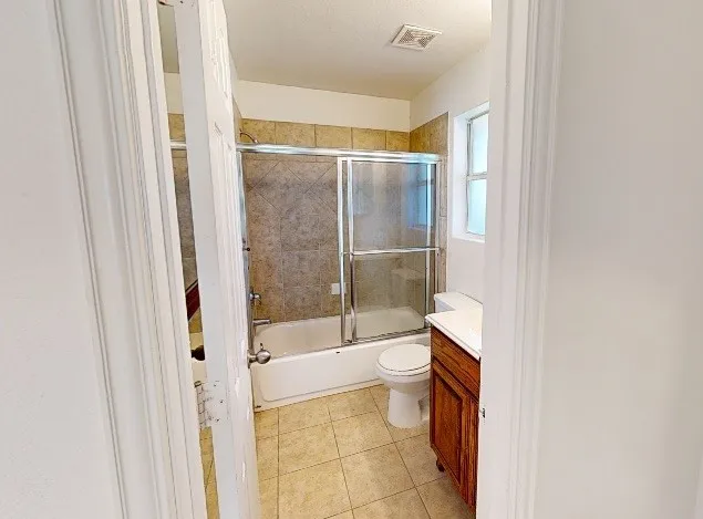 Bathroom featuring a shower-tub combination with sliding glass doors, tile surround, and a compact vanity with a built-in sink