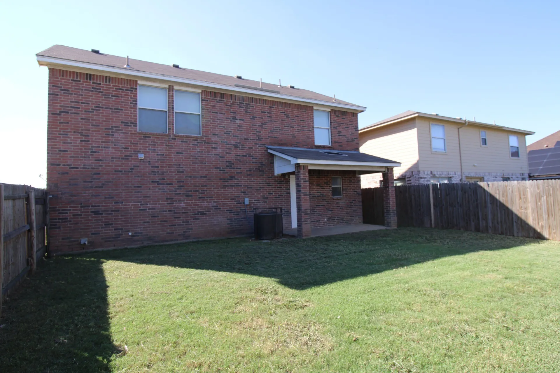 Brick exterior featuring a covered patio, a fenced backyard, and an upper-level window