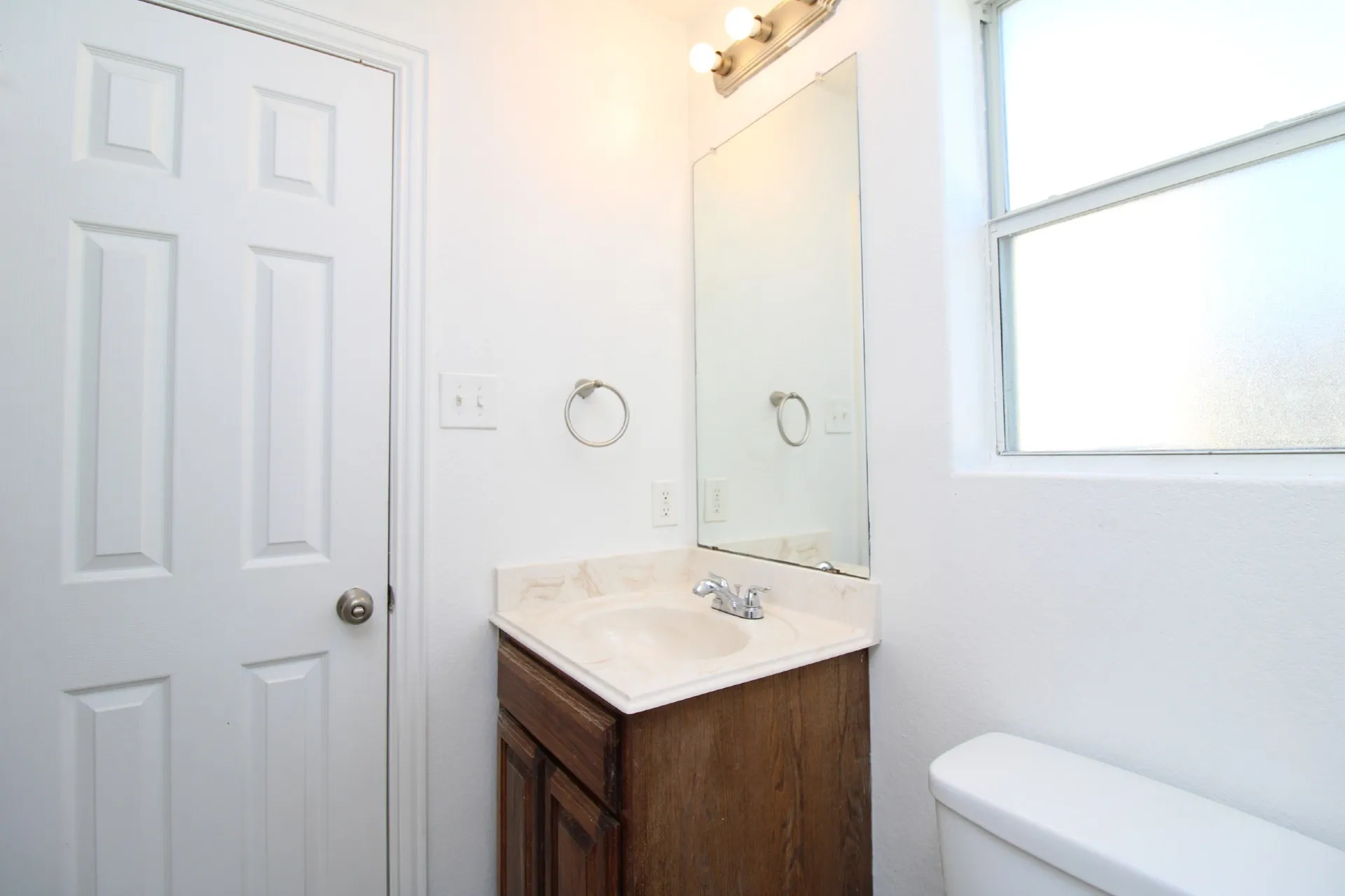 Bathroom featuring a built-in vanity with a countertop sink, a wall-mounted mirror, overhead lighting, a toilet, and a window