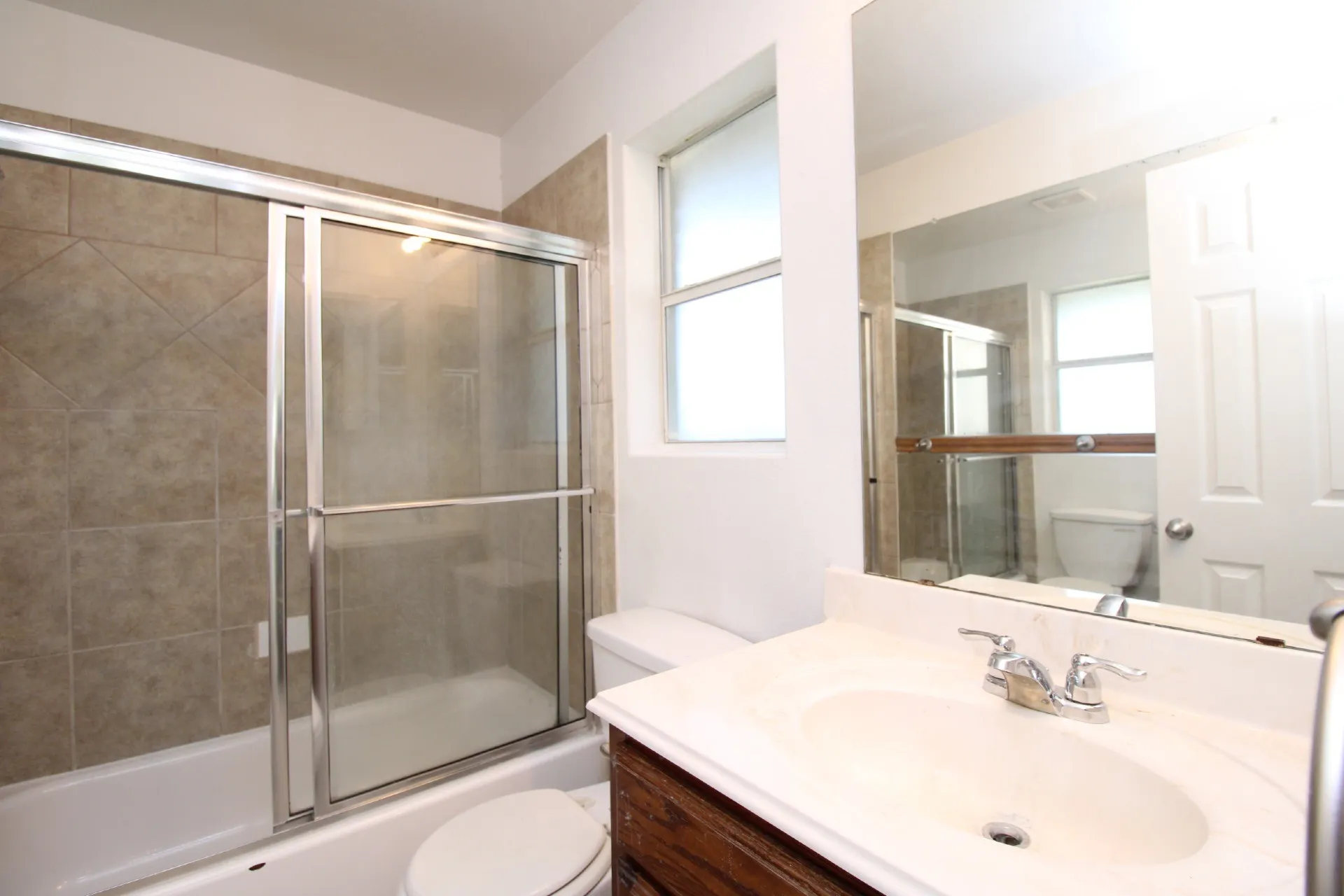 Tub and shower combination with sliding glass doors, tile surround, white vanity with integrated sink, chrome faucet, and large wall-mounted mirror