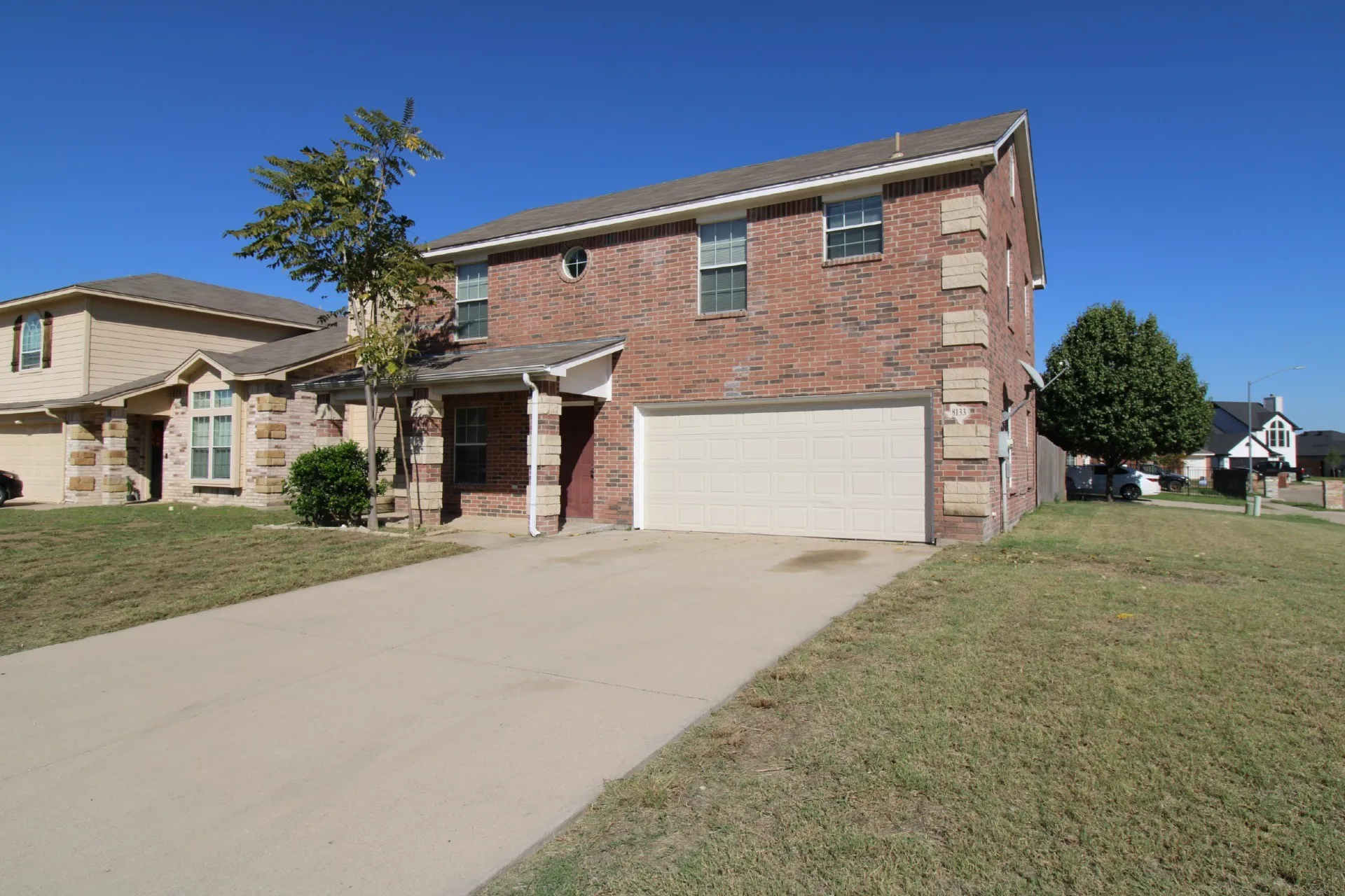 Brick exterior with stone accents, two-story construction, attached garage, concrete driveway, and front entry porch