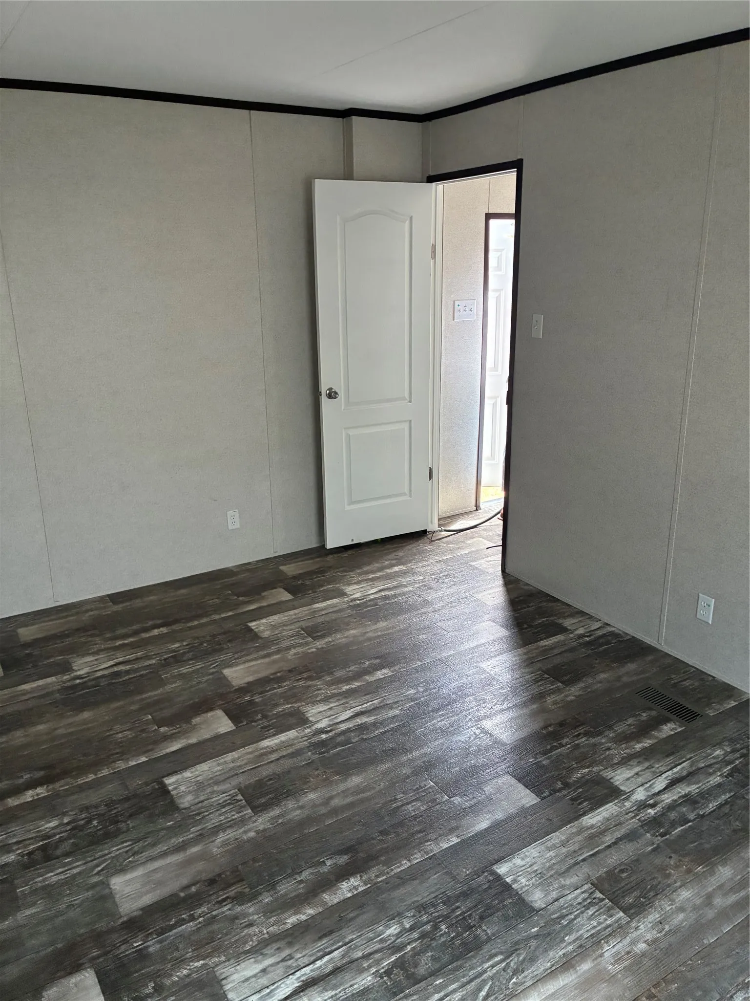 Wood-finish flooring with varied grey tones, light-toned wall panels, white interior door, and dark trim details