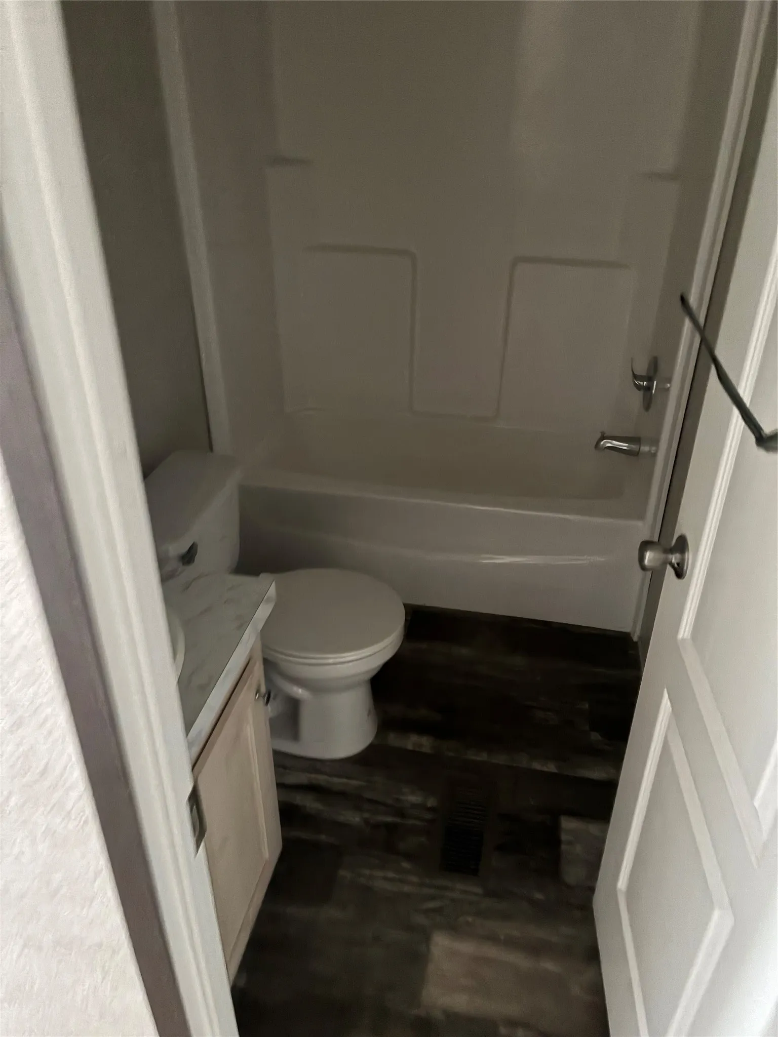 Bathroom featuring a white bathtub and shower combination, a white toilet, a vanity with a light wood-finish cabinet, and dark wood-finish flooring