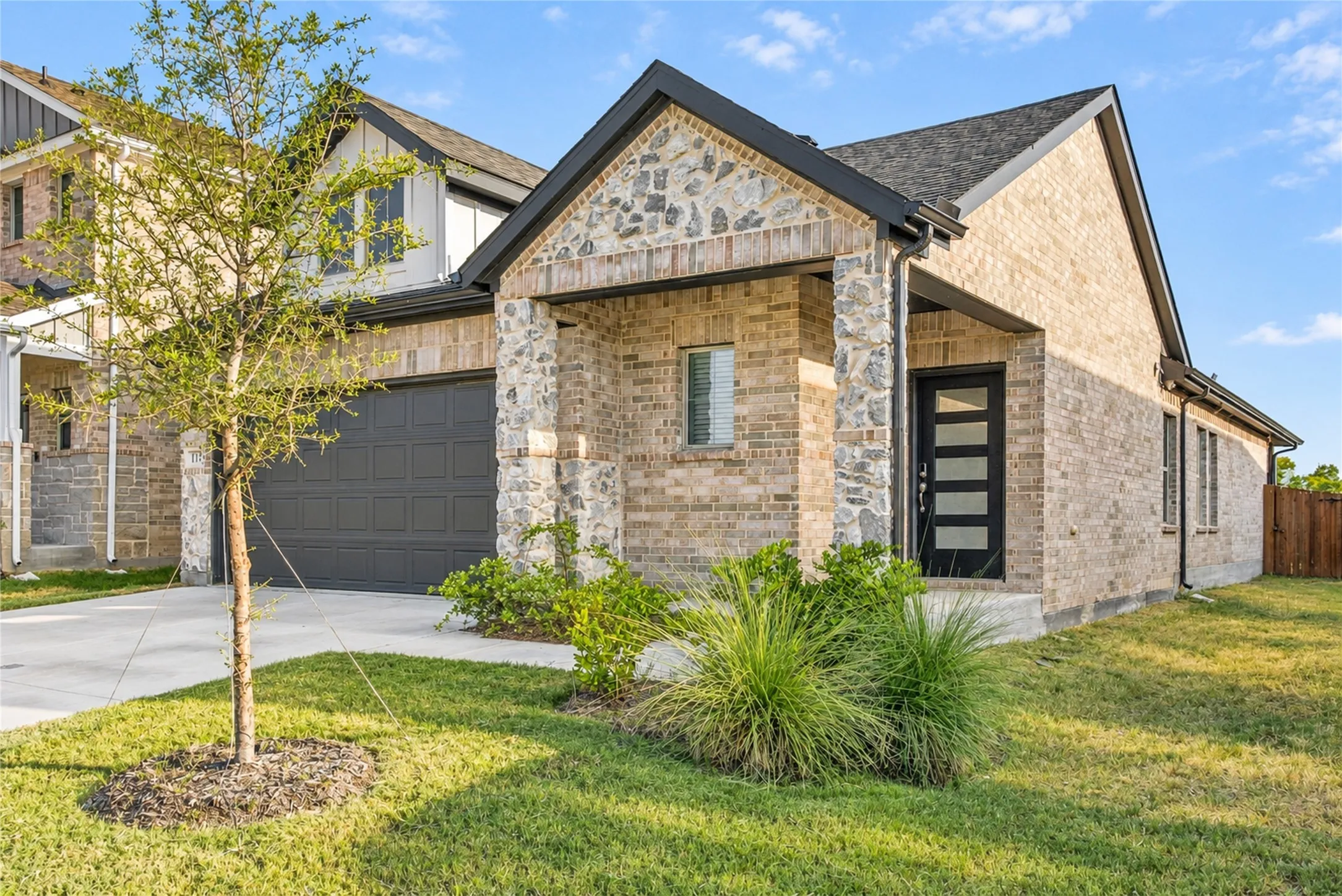 Brick and stone facade, dark-framed entry door with frosted glass panels, attached two-car garage, established front landscaping, and a concrete driveway