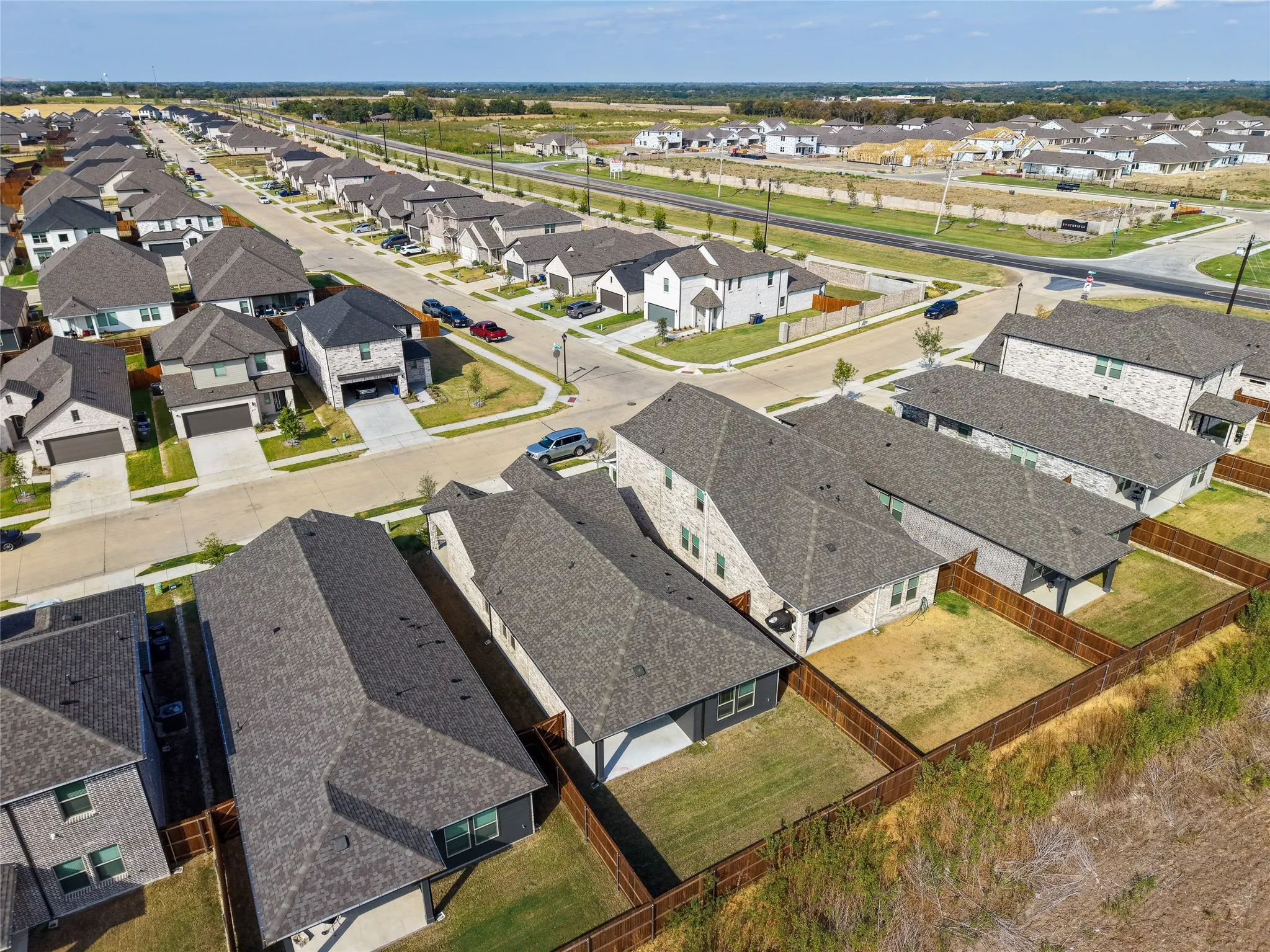 Residential neighborhood street with multiple two-story homes, brick and siding exteriors, attached garages, and fenced backyards