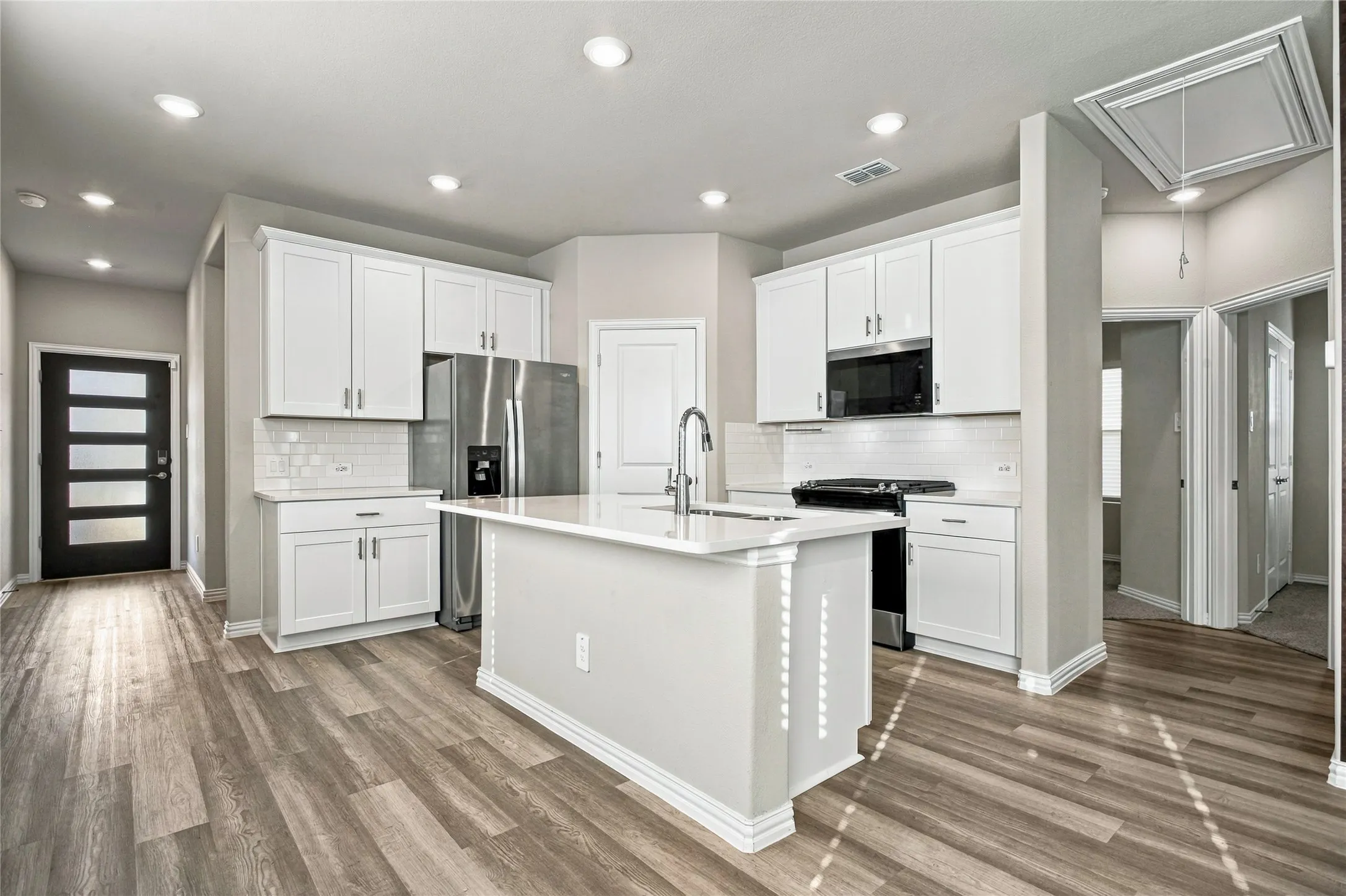 Kitchen featuring an island with a sink, stainless steel appliances, white cabinetry, recessed lighting, and wood-finish flooring