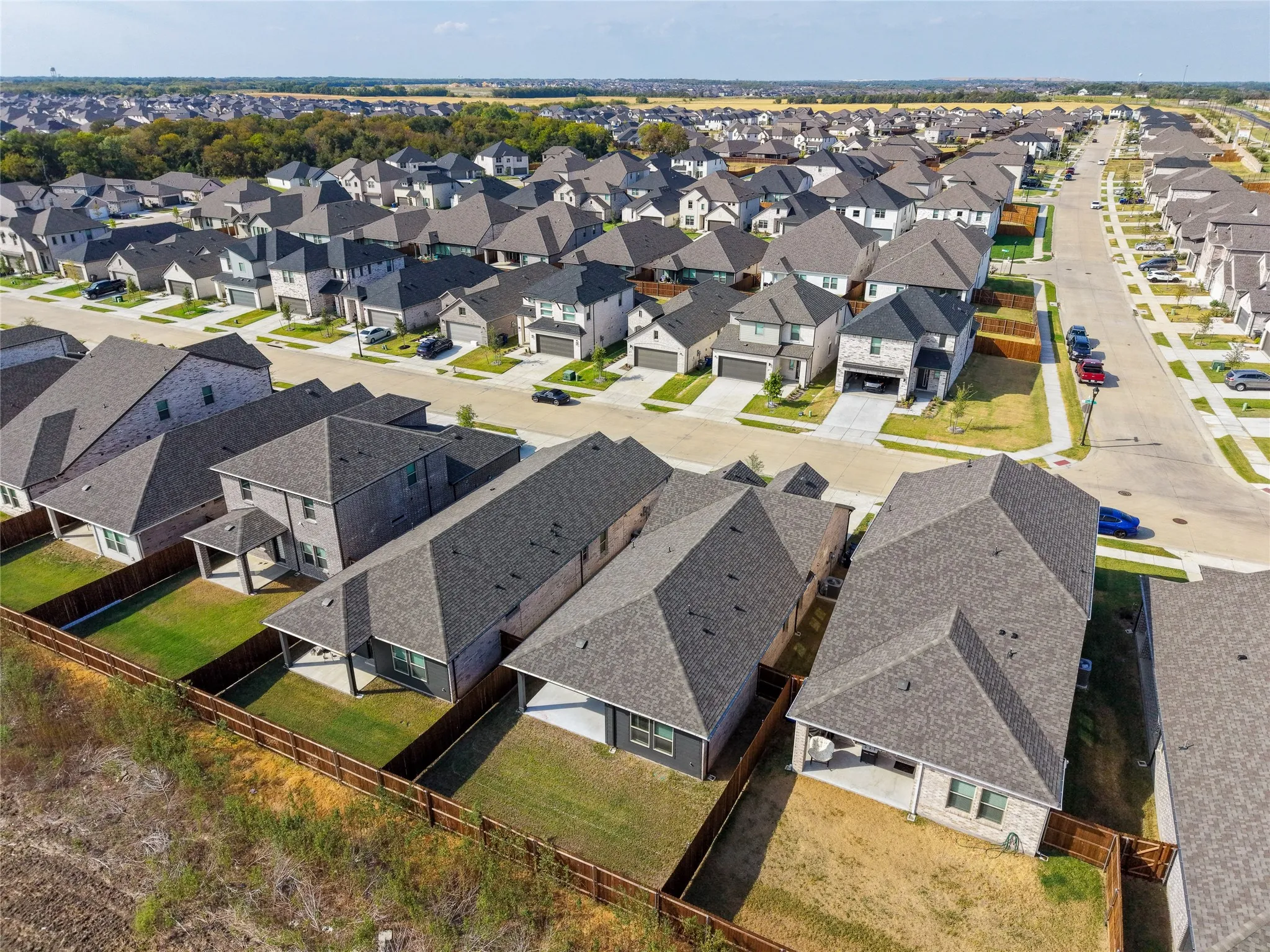 Aerial perspective of a residential neighborhood featuring multiple single-family homes with gray shingle roofs, private fenced yards, and concrete driveways