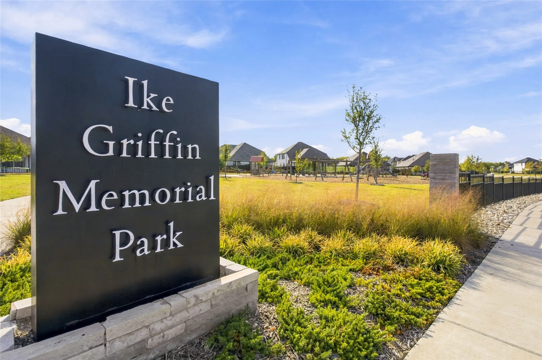 Black monument sign with "Ike Griffin Memorial Park" lettering, stone base, concrete pathway, and landscaped grounds with grass and plantings