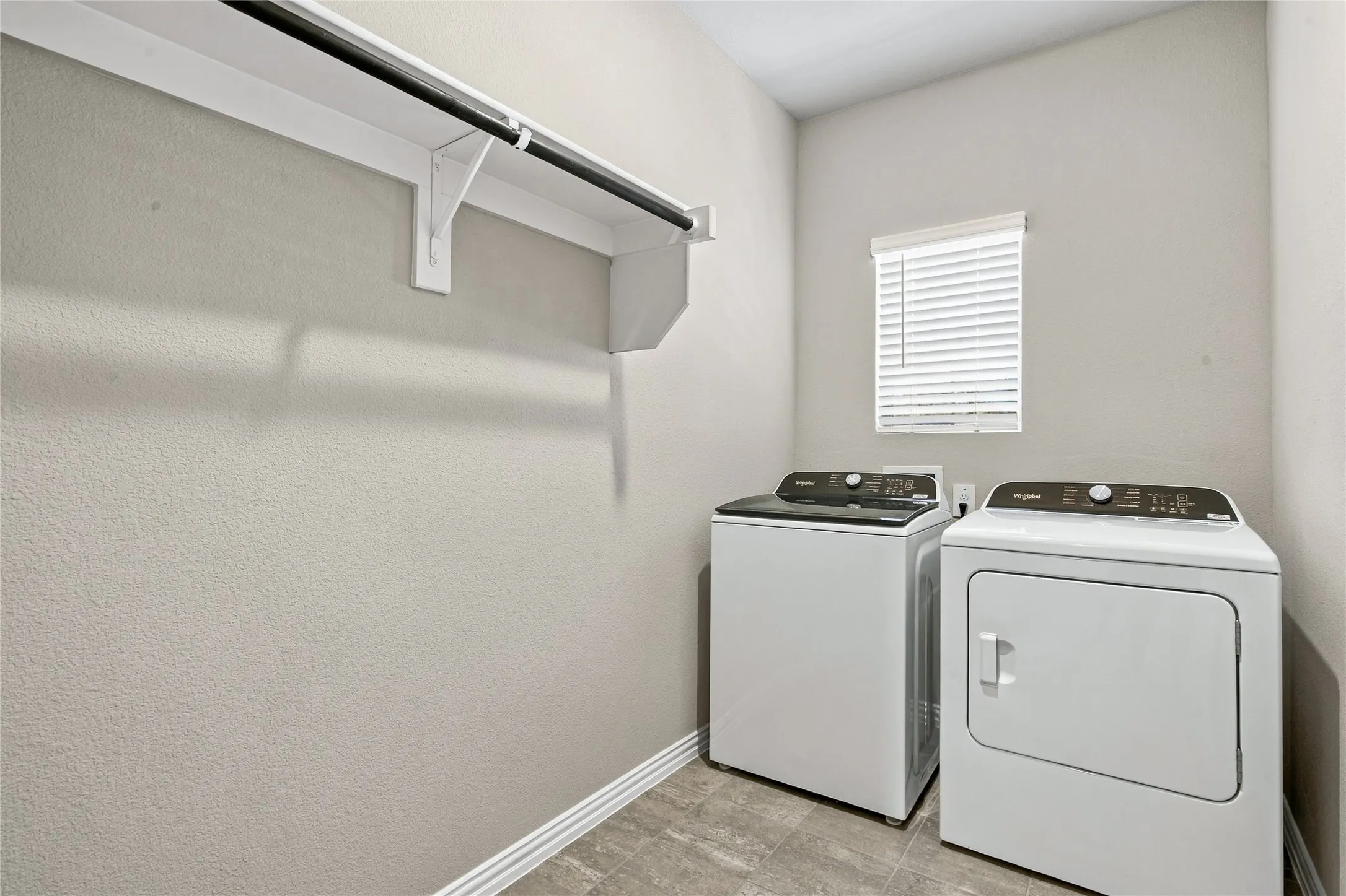 White shelving with a dark-finish hanging rod, neutral-toned walls, and wood-finish flooring