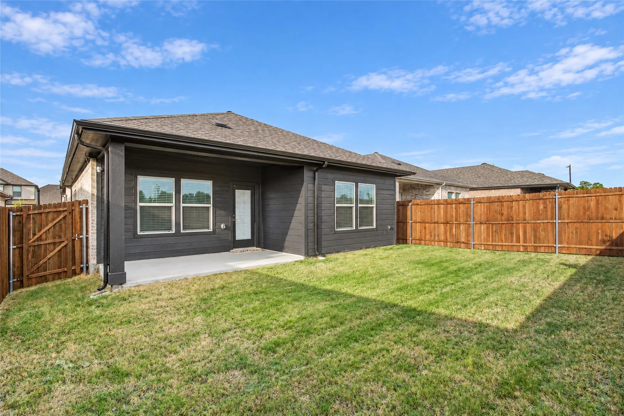 Expansive backyard with a covered concrete patio, wood privacy fencing, and a manicured lawn