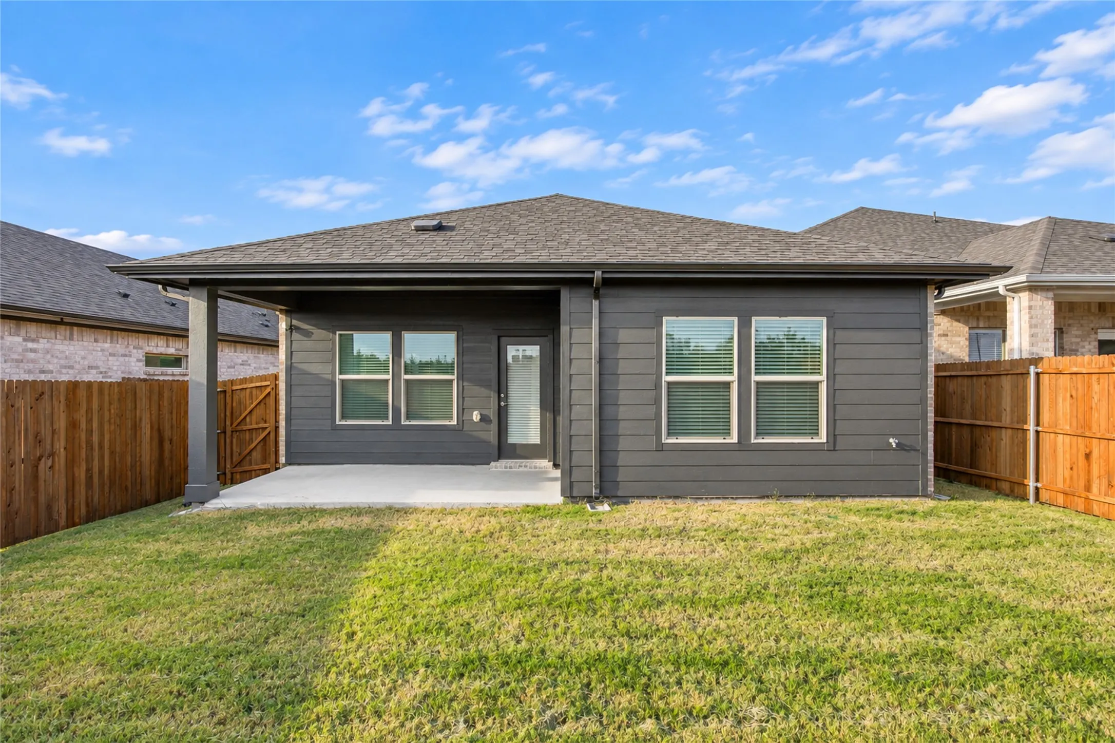 Spacious backyard with a covered patio, dark gray siding, and a wooden privacy fence