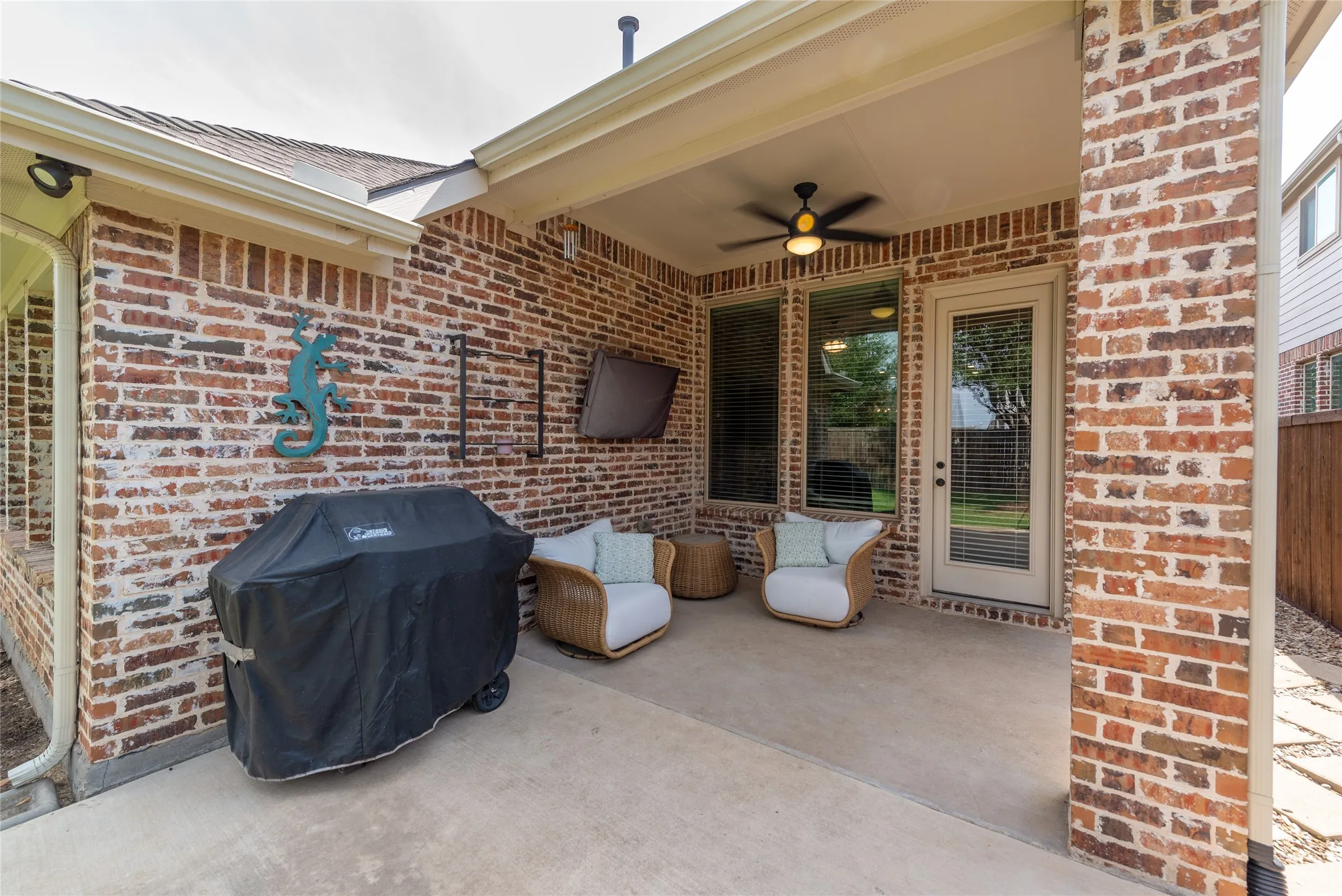 Covered patio featuring a ceiling fan, brick exterior, concrete flooring, and an exterior door with louvered blinds