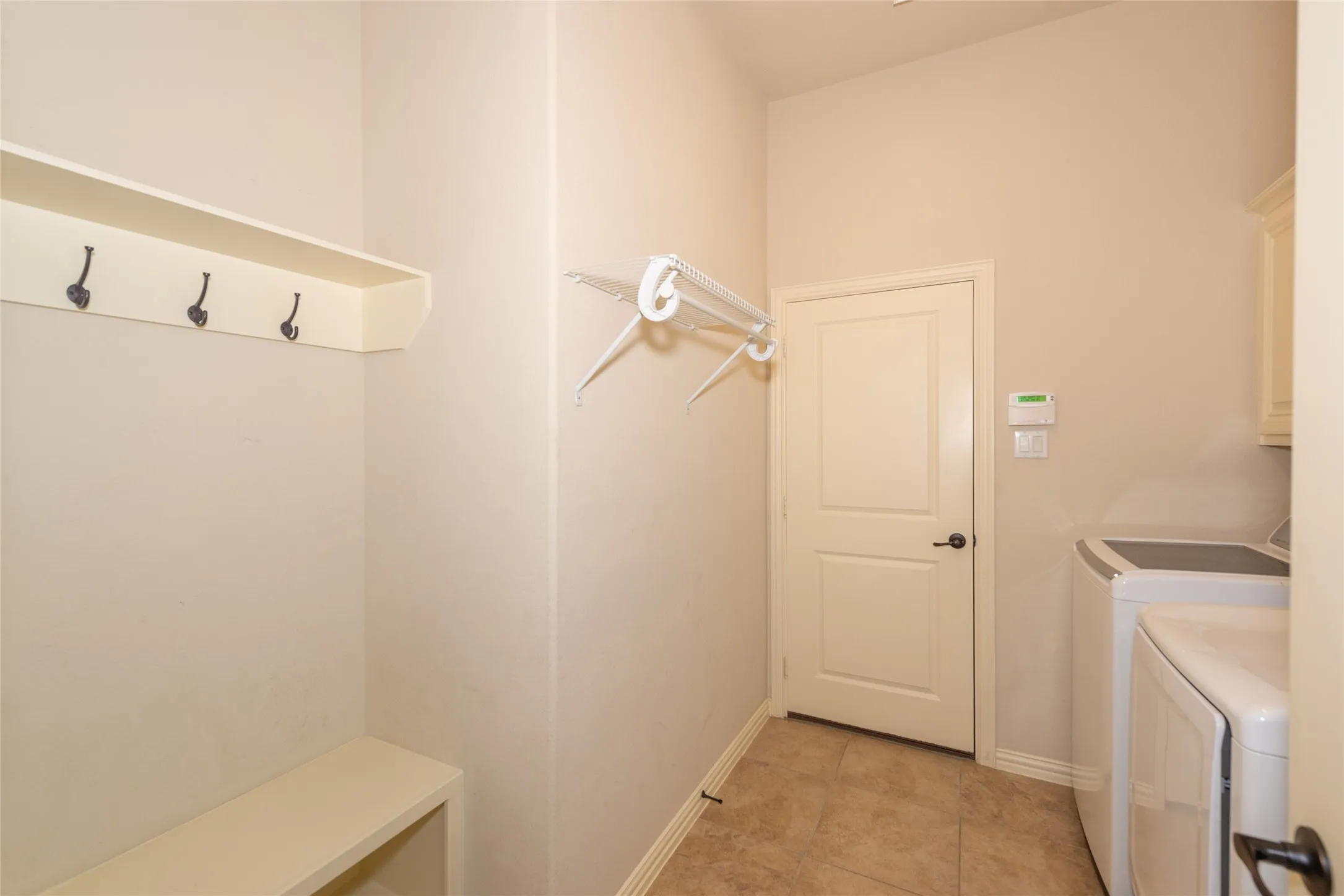 Laundry area featuring tile flooring, built-in shelving with coat hooks, and clothes drying rack
