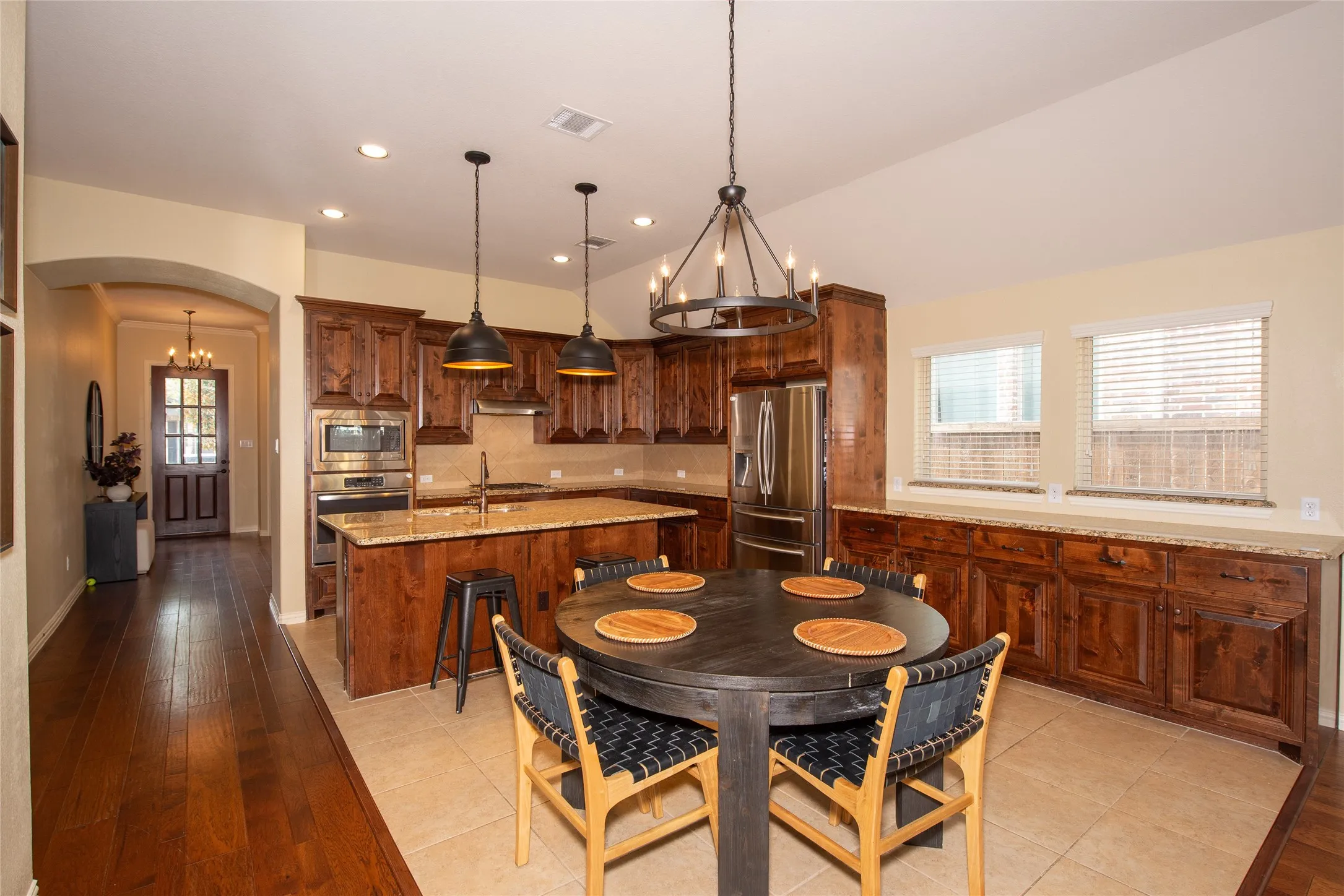 Kitchen with wood-finish cabinetry, stainless steel appliances, a center island with sink, and tile flooring