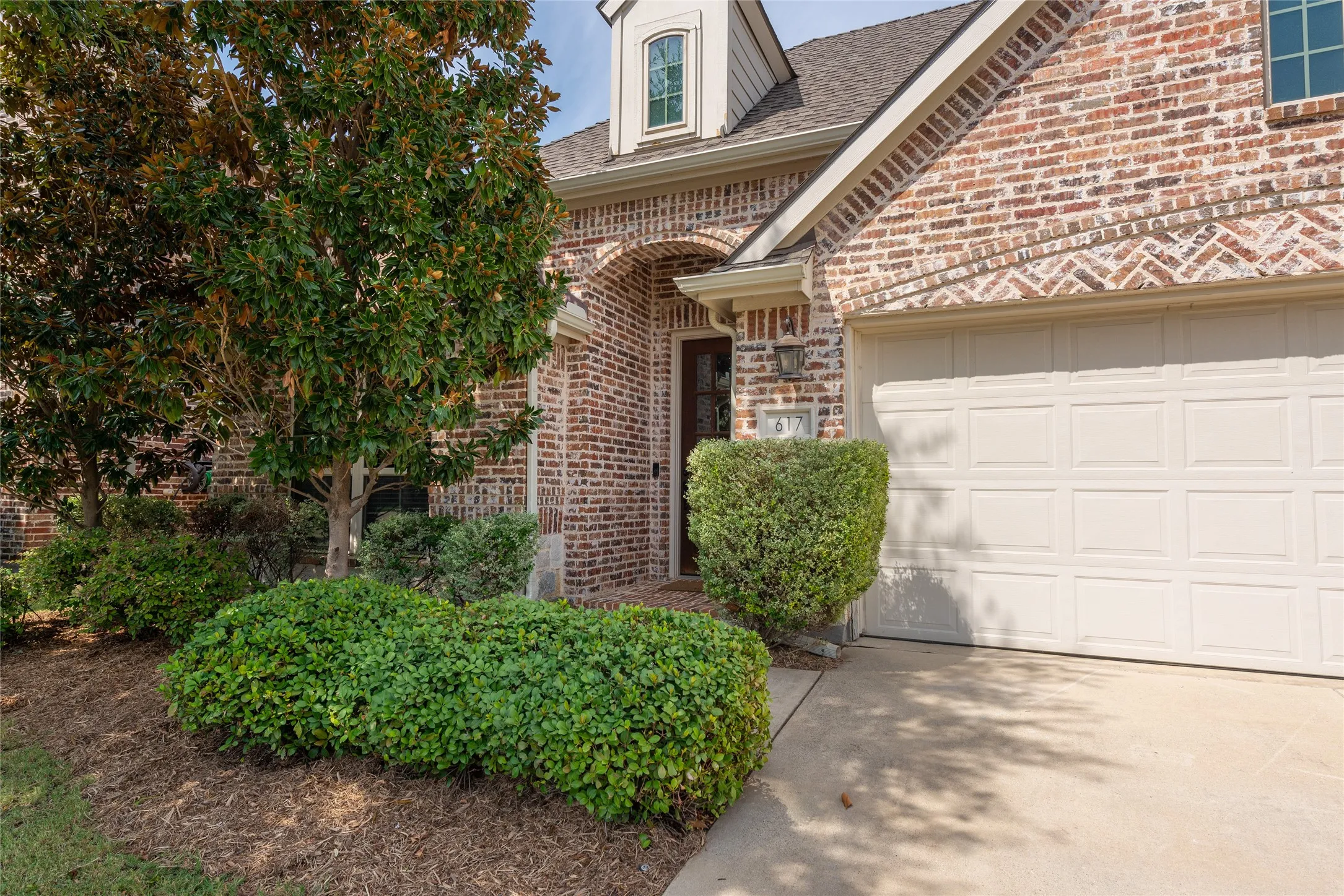 Brick exterior with an arched entryway, dormer window, and an attached garage