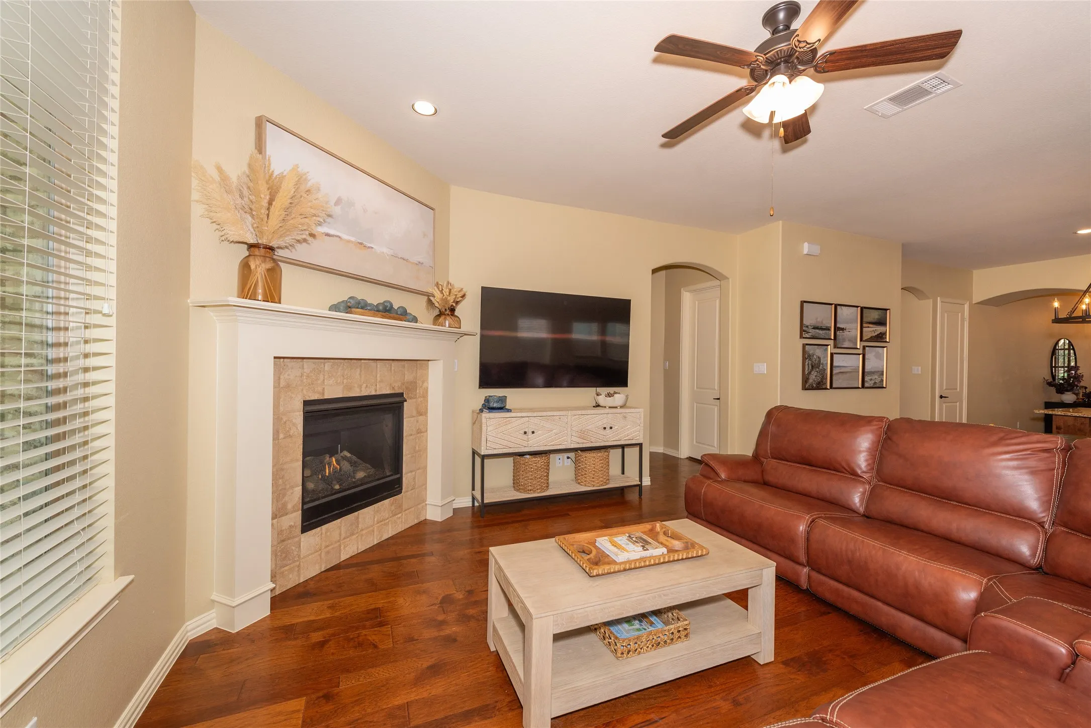 Fireplace with tile surround and mantel, wood-finish flooring, recessed lighting, ceiling fan, and arched doorways