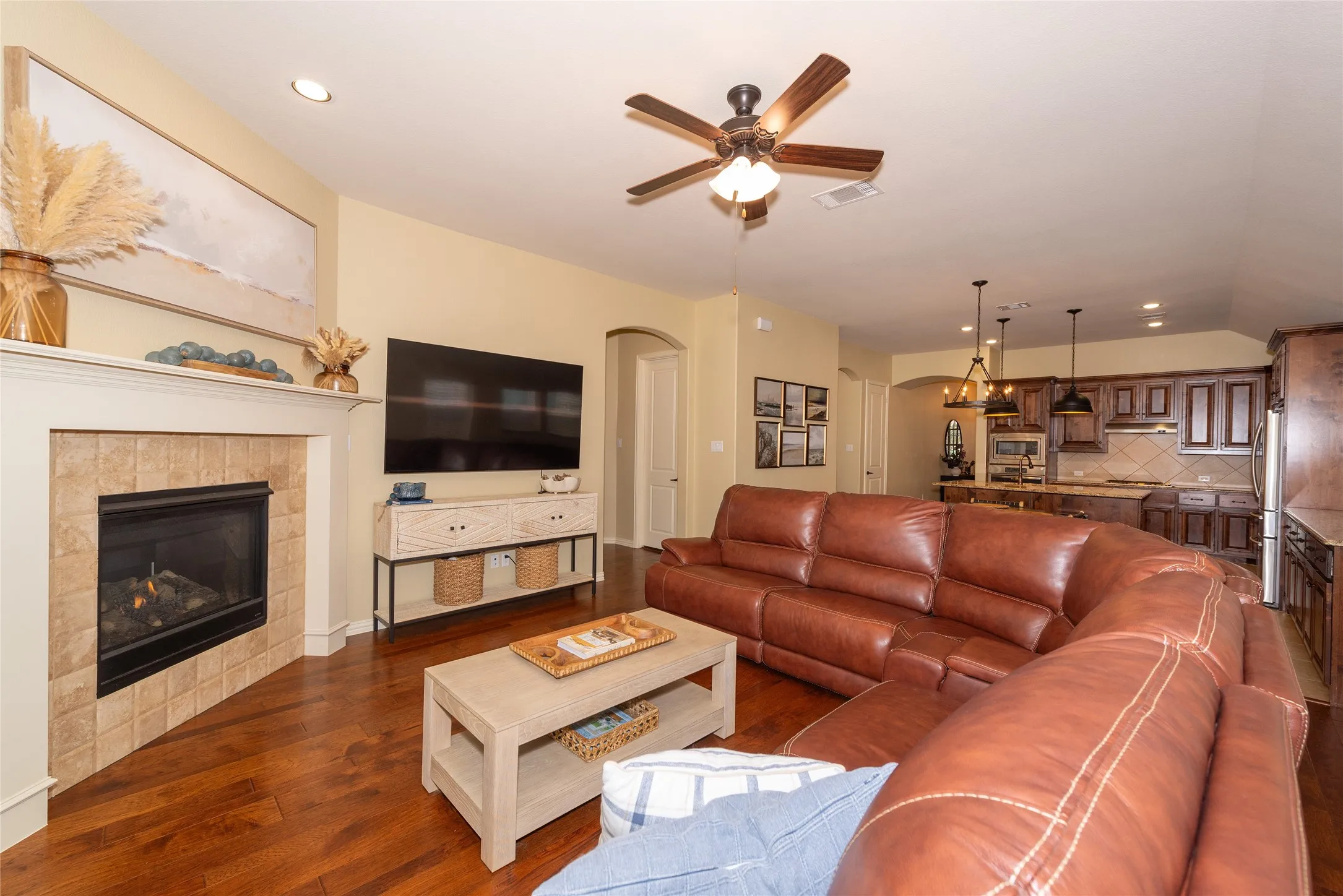 Spacious living room featuring a custom leather sectional sofa, wood-finish flooring, and a gas fireplace with tile surround