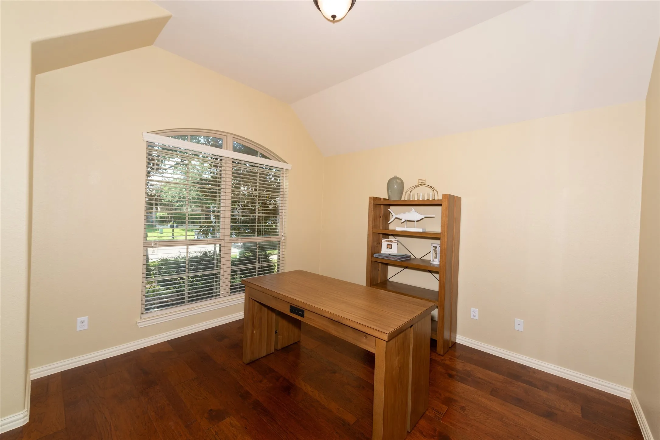 Vaulted ceiling with an arched window and wood-finish flooring