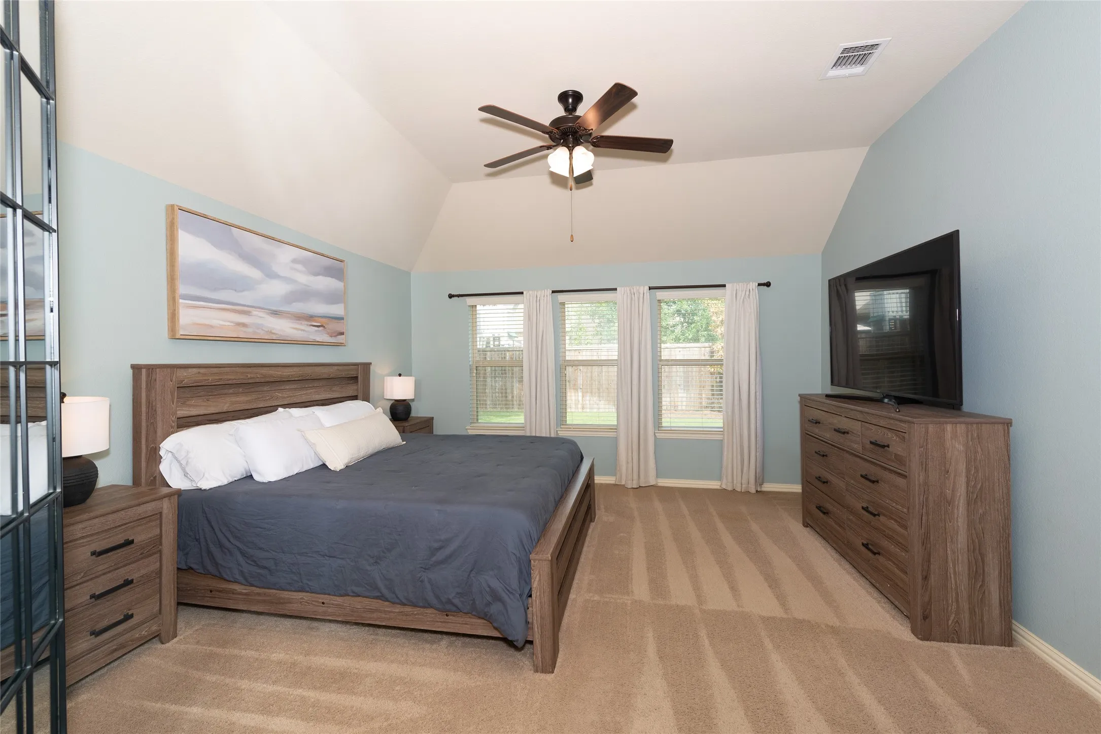 Vaulted ceiling, three windows, ceiling fan, wood-finish flooring, and light blue wall color