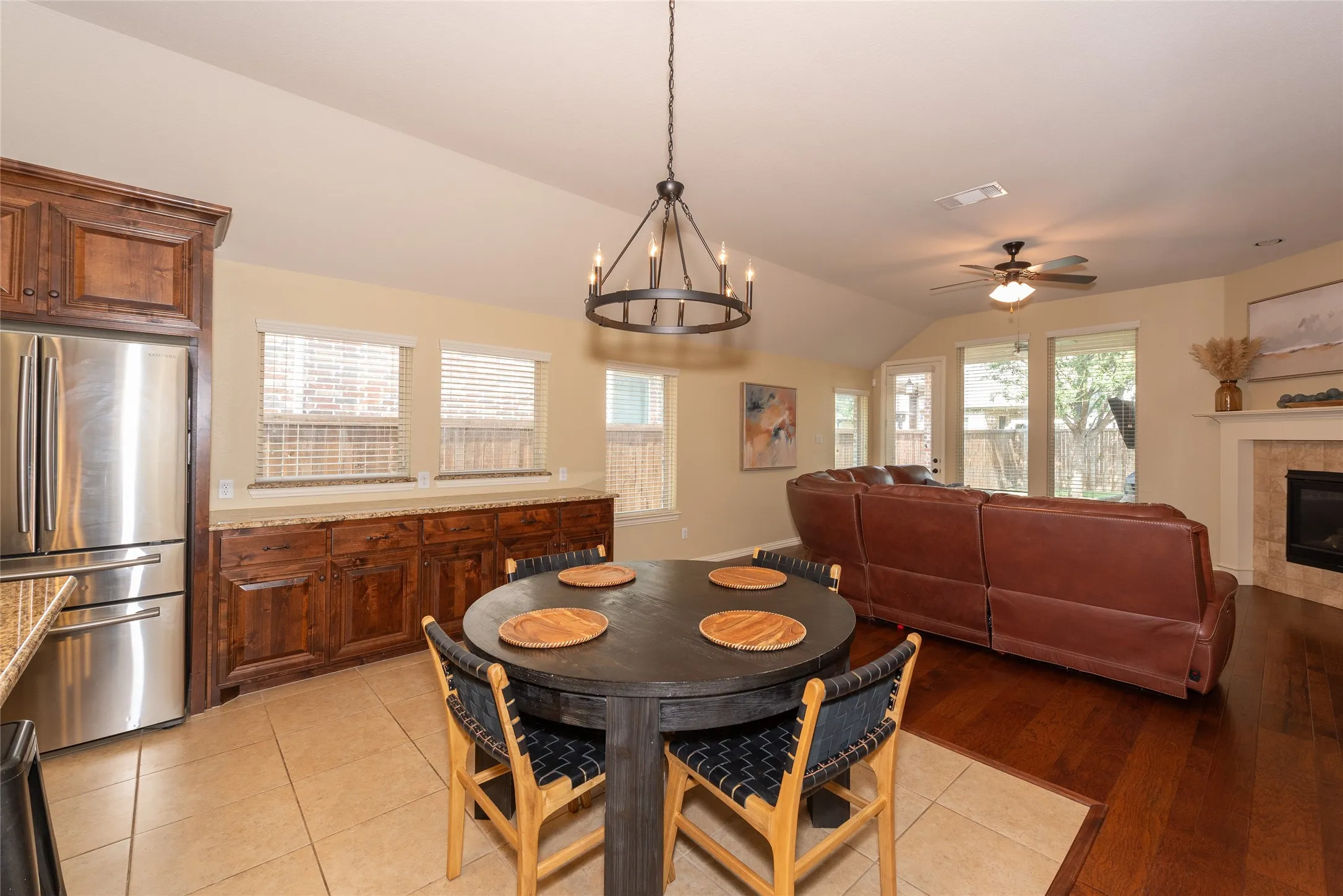 Vaulted ceiling, wood-finish flooring, custom wood cabinetry, stainless steel refrigerator, and a built-in fireplace
