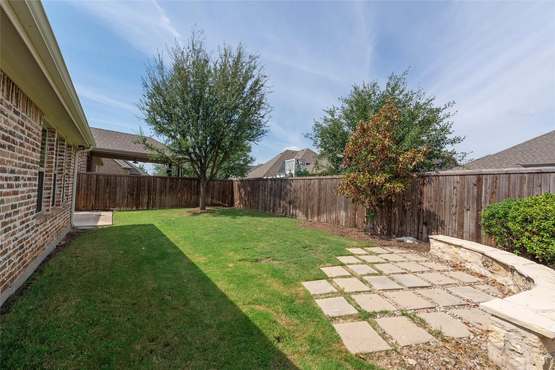 Expansive backyard featuring a manicured lawn, stone paver patio, stone retaining wall, and wood privacy fencing