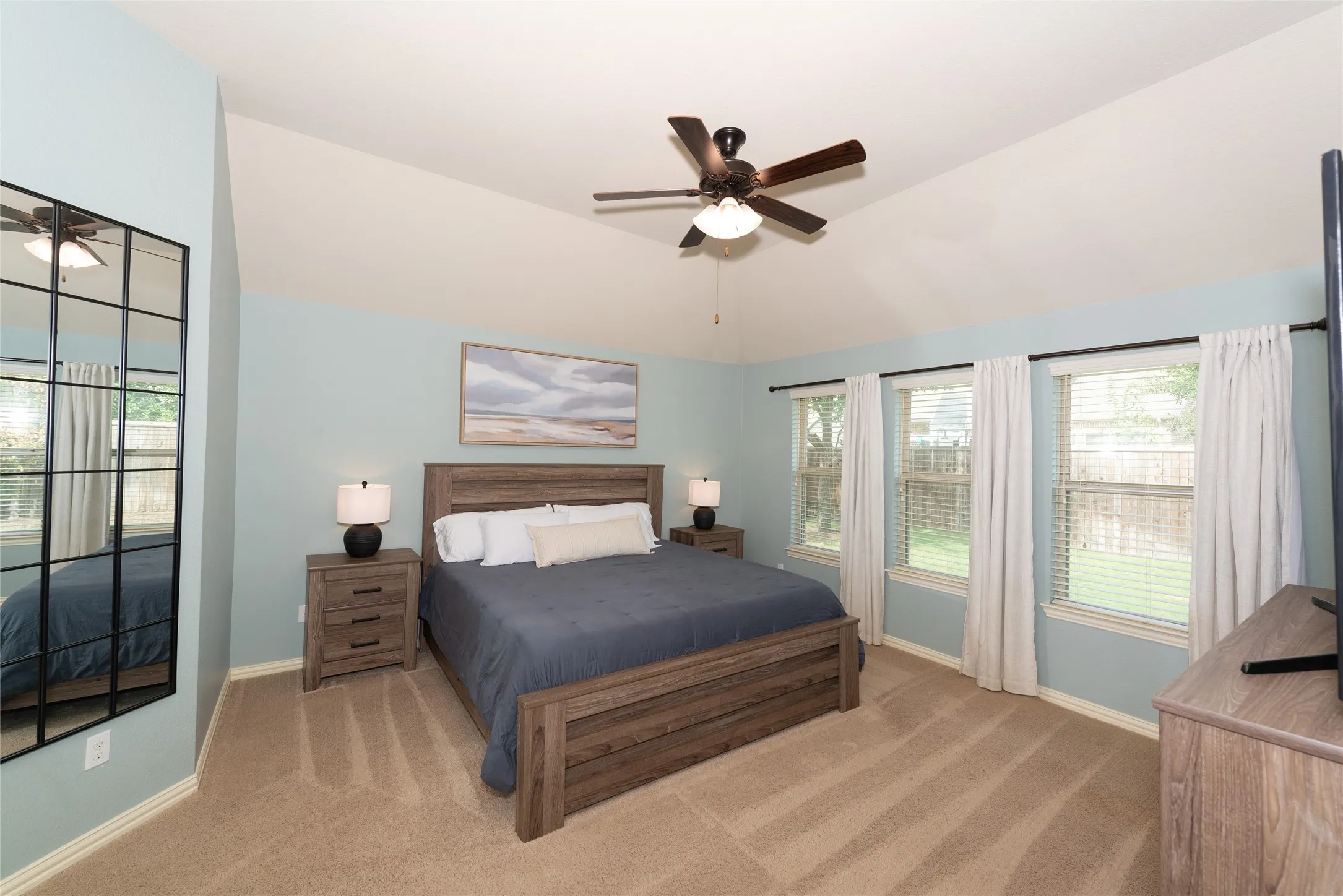 Vaulted ceiling with a ceiling fan, three windows, and carpet flooring